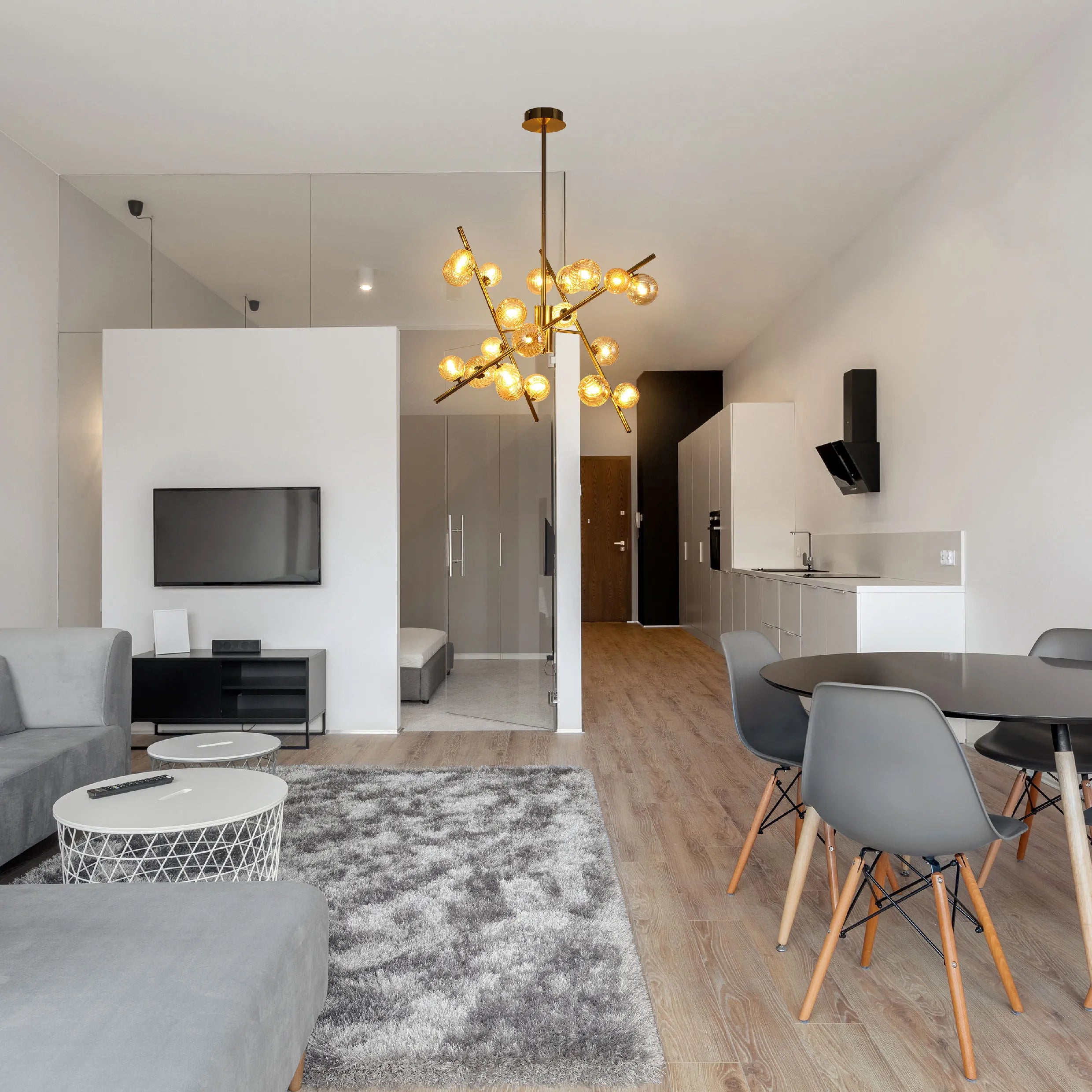 A modern living space, illuminated by a striking gold chandelier with glowing glass bulbs. The sleek design complements the contemporary interior.