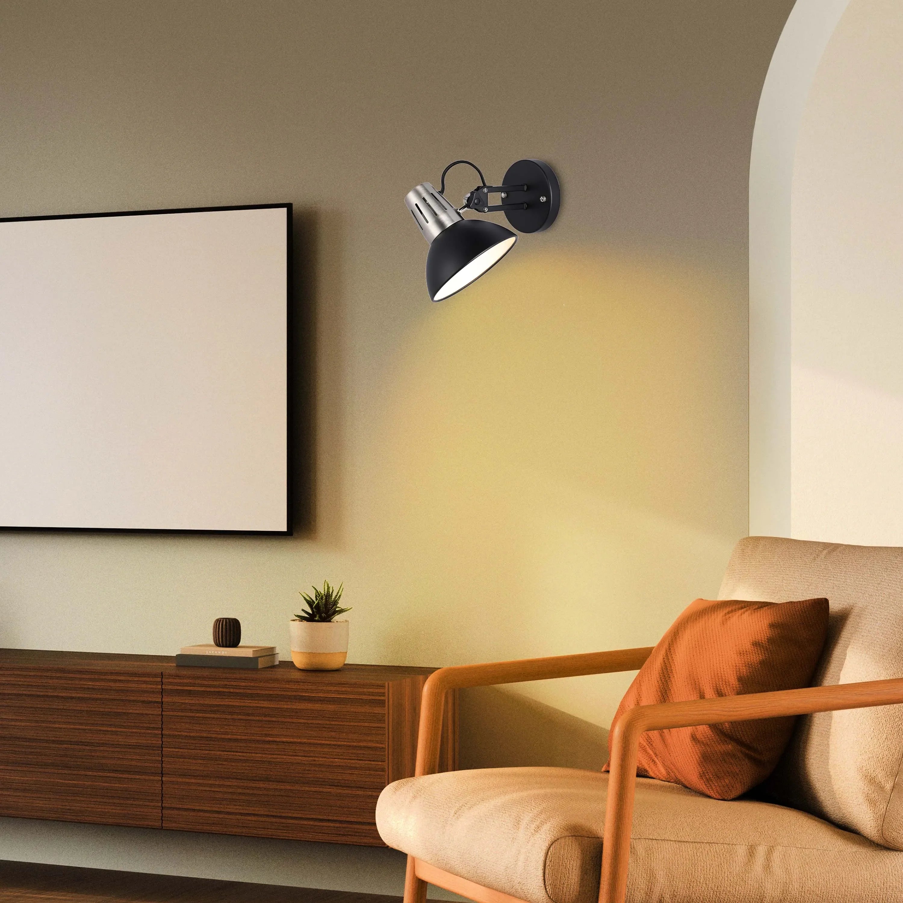 An adjustable black and silver wall light illuminates a cosy living space with a warm glow, highlighting the modern decor.