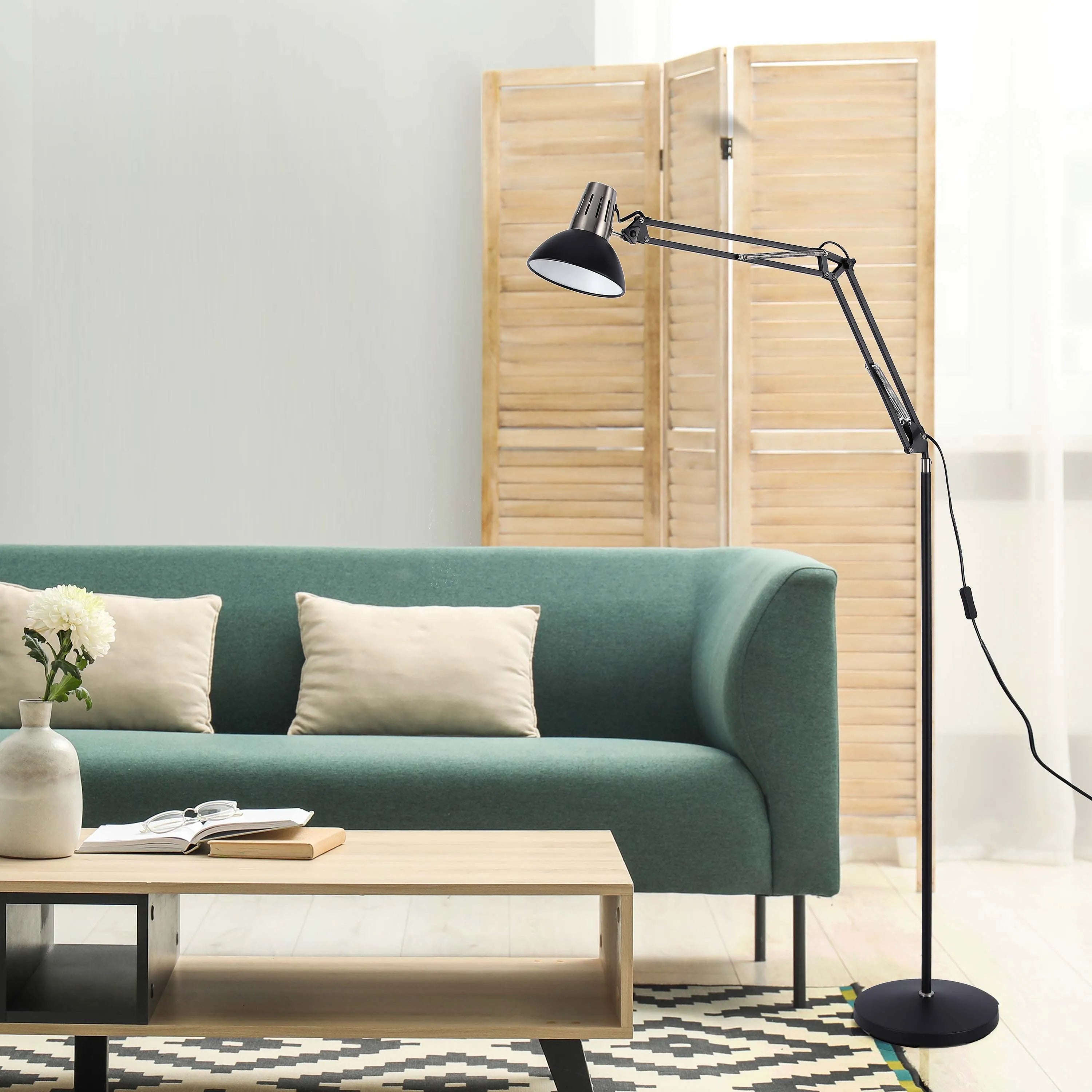 A black articulated floor lamp illuminates a modern living room with a green sofa and wooden coffee table.