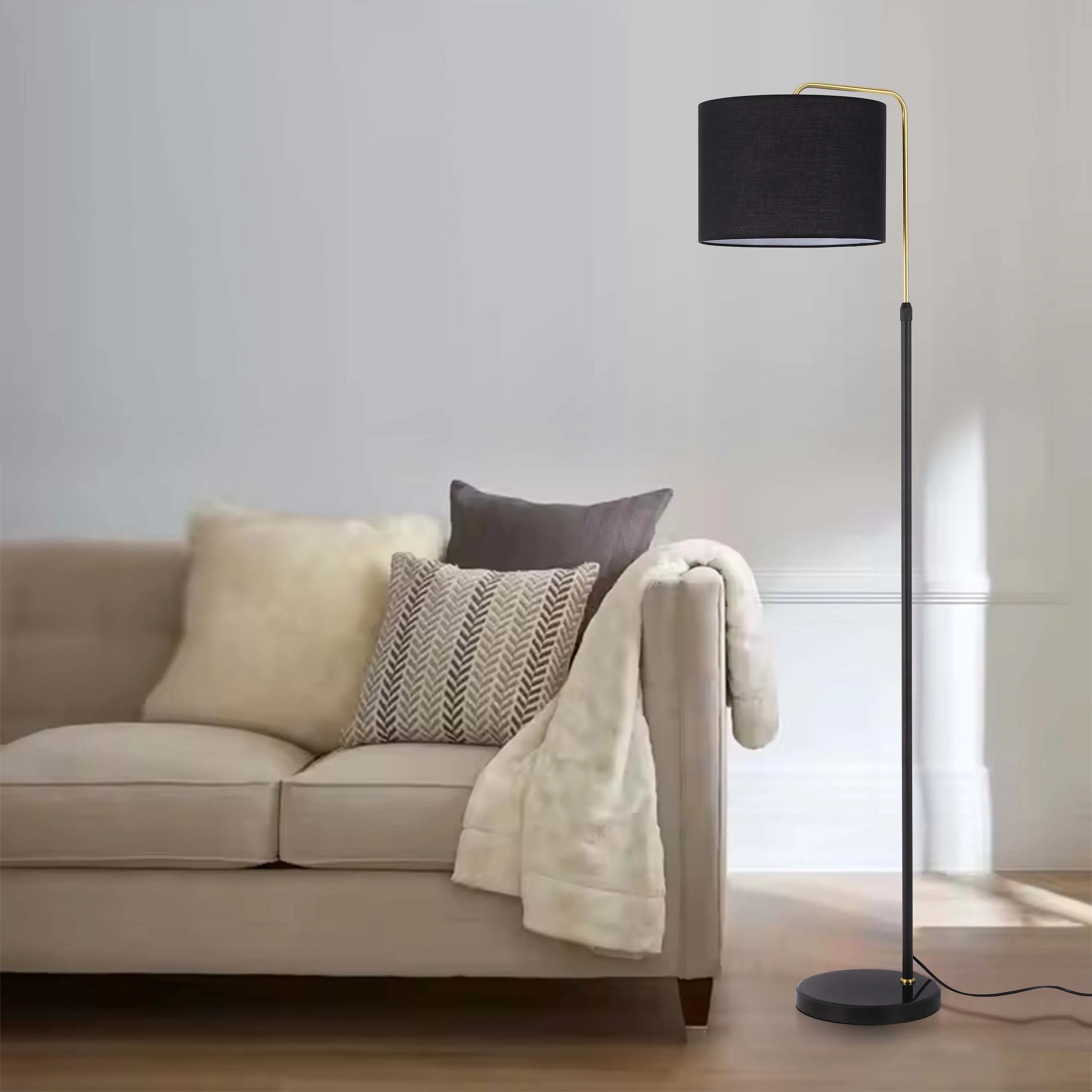 A modern black and gold floor lamp illuminates a beige sofa with cushions. A stylish lighting choice for a living room.