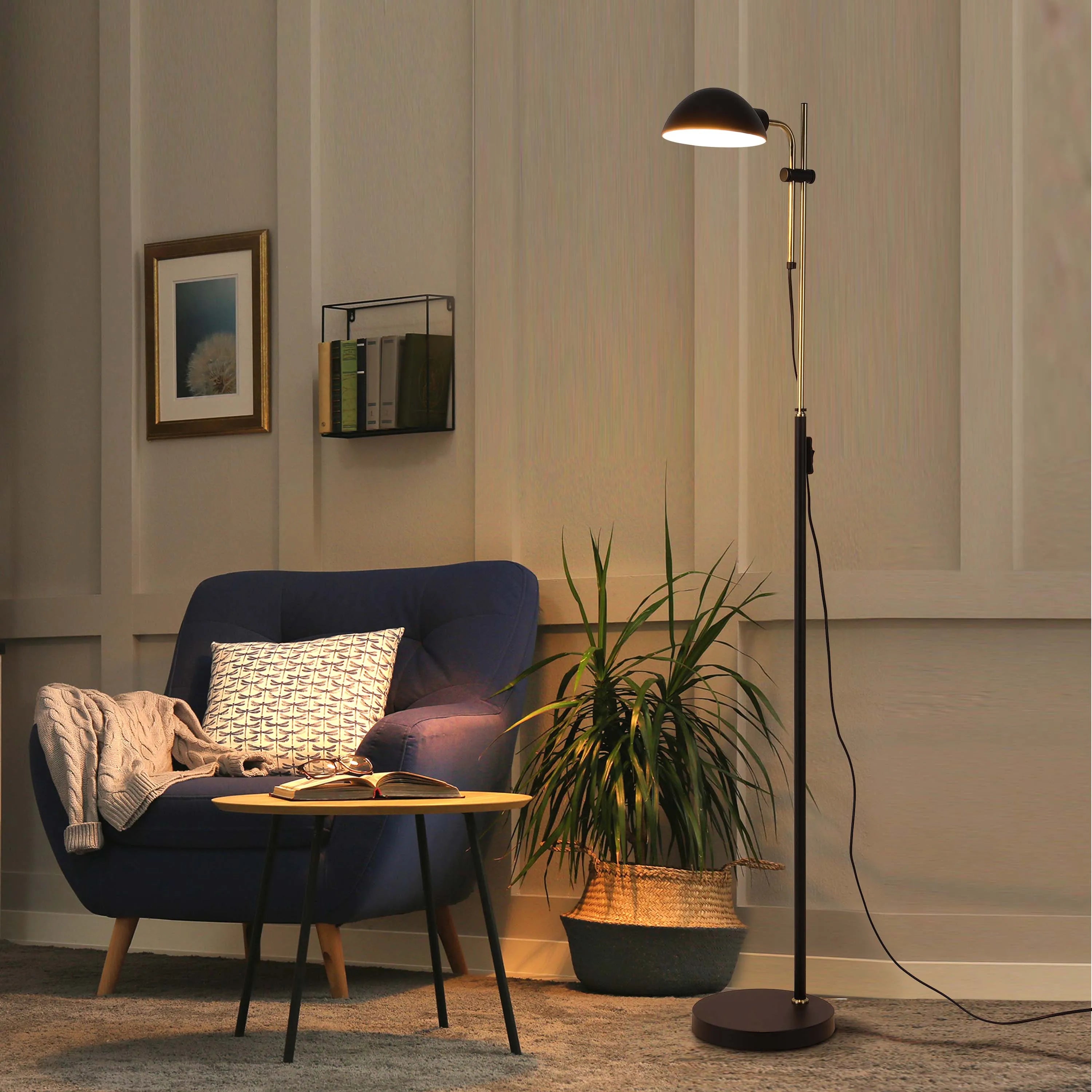 A modern floor lamp illuminates a cosy reading nook with an armchair, side table, potted plant, and framed print. Warm and inviting.