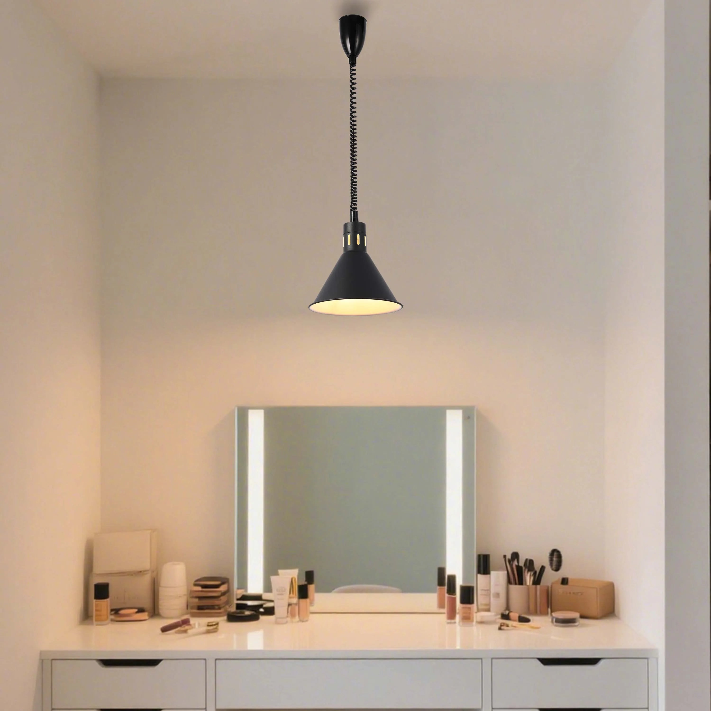 A black pendant light illuminates a dressing table. The light is suspended with a coiled cable. The mirror also has built in lights.
