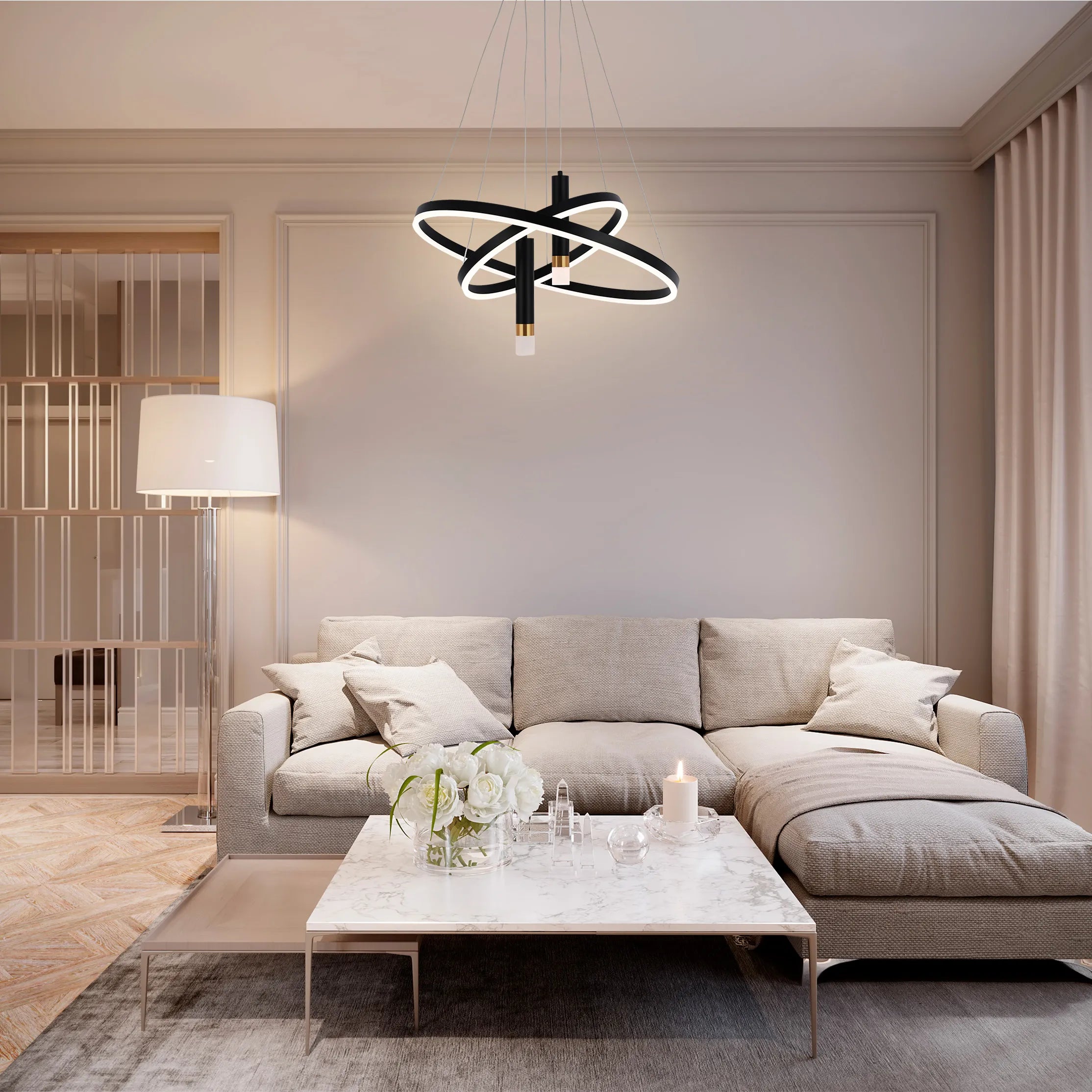 A modern living room is lit by a stylish, multi-tiered black and white LED chandelier and a floor lamp. Warm lighting creates a cosy atmosphere.