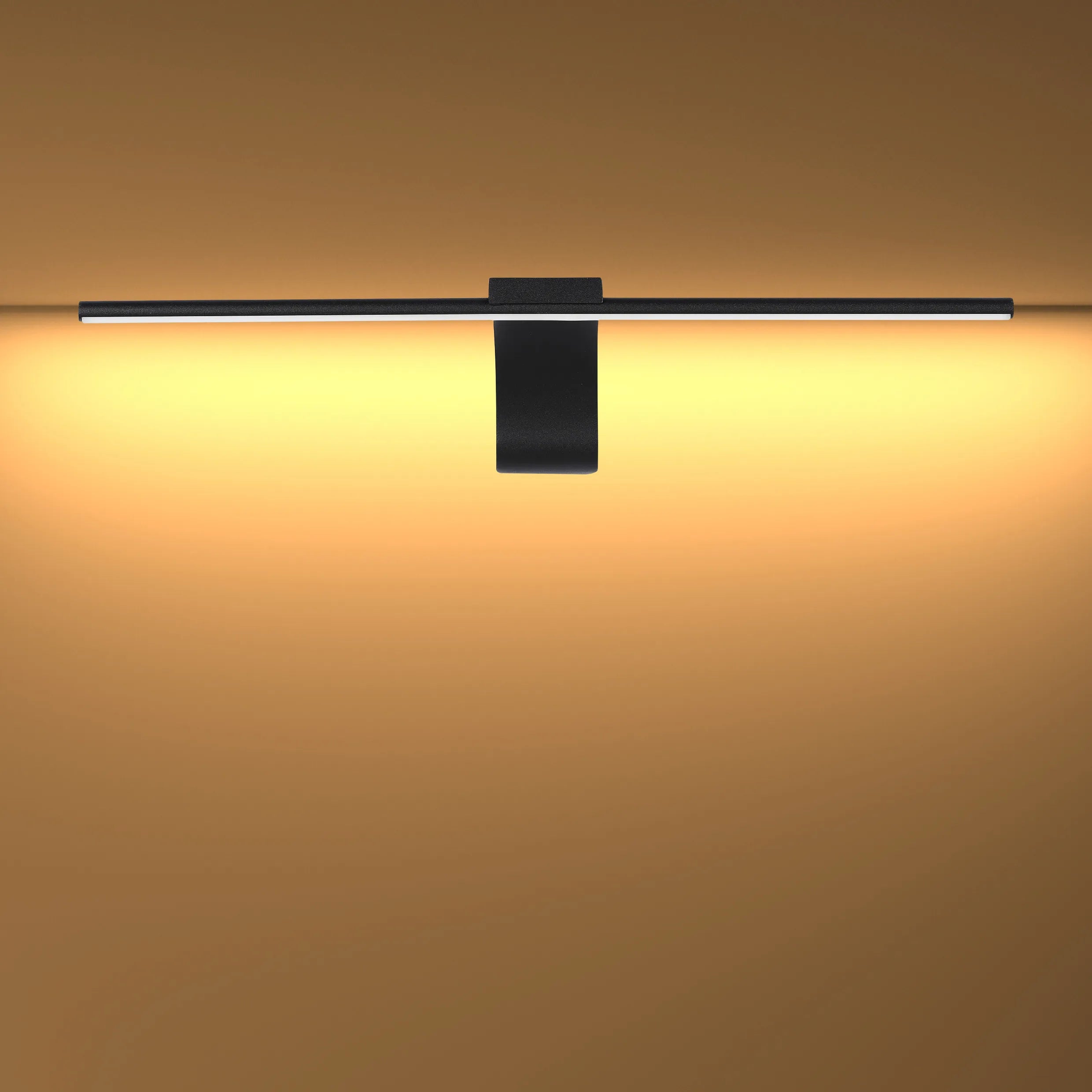 Black wall mounted linear LED light fixture emitting warm, ambient light onto the wall. Minimalist lighting design.