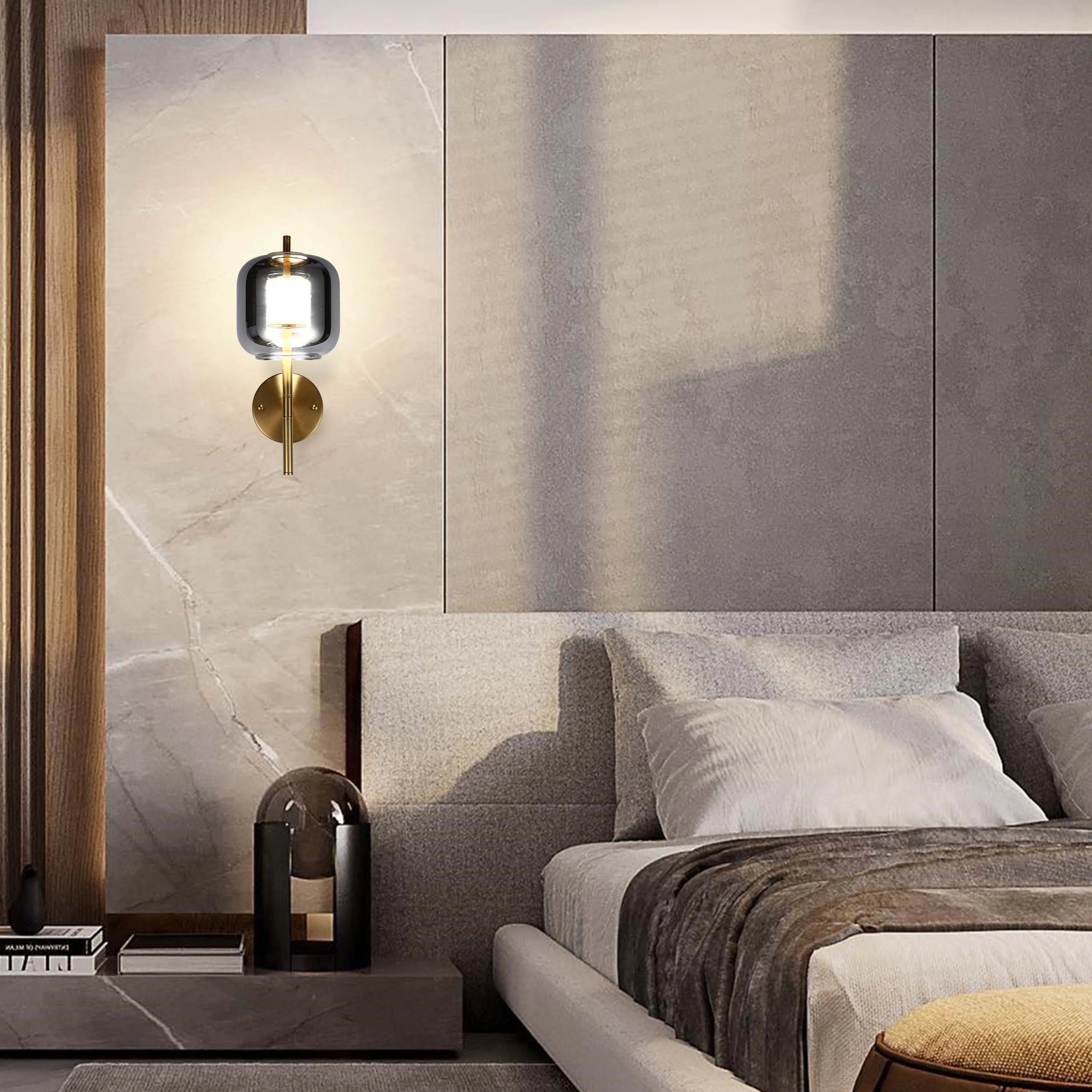 A modern grey glass wall light with a gold fitting, providing an ambient glow for a cosy bedroom space.