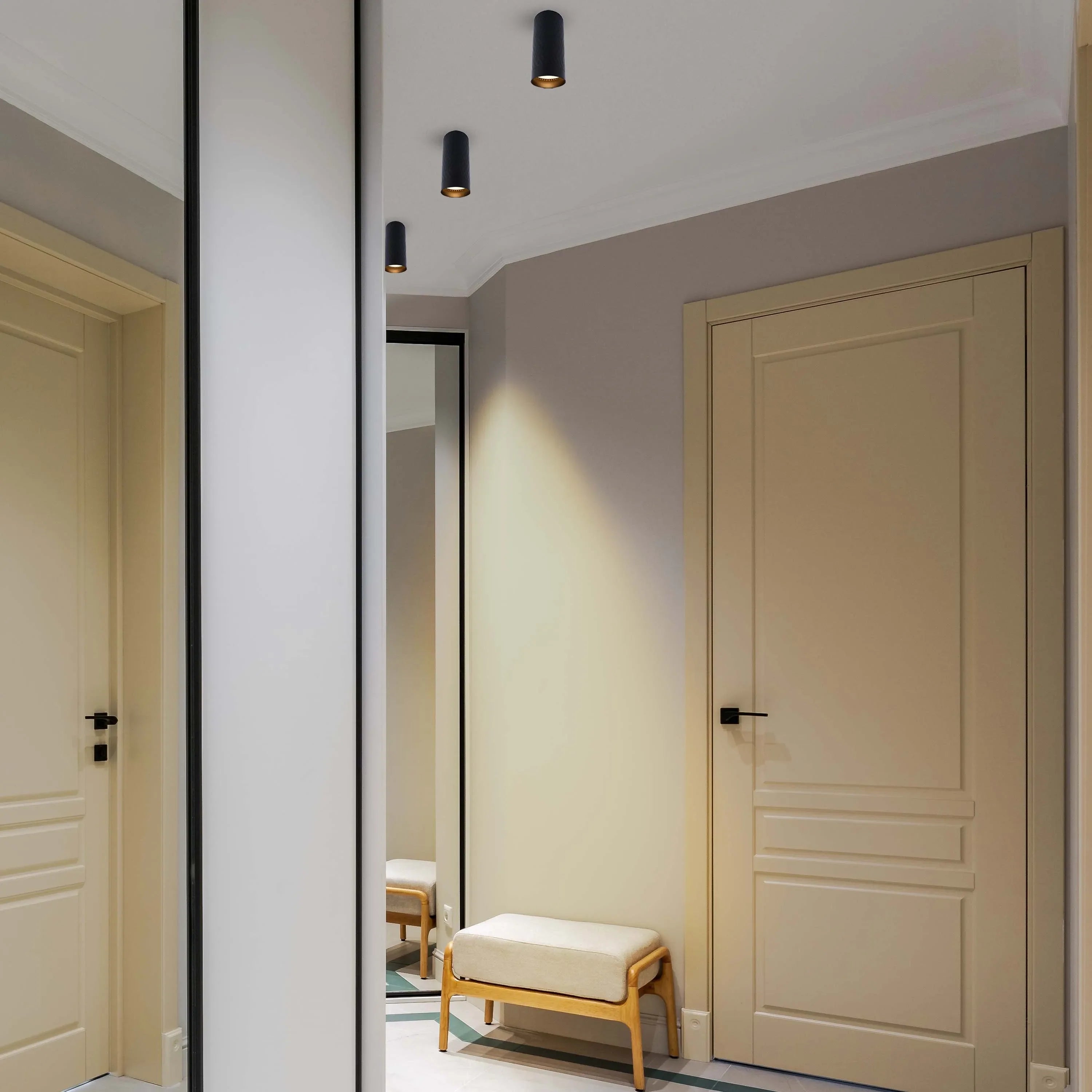 Contemporary black cylinder downlights provide focused pools of light in this hallway, complementing the neutral decor.