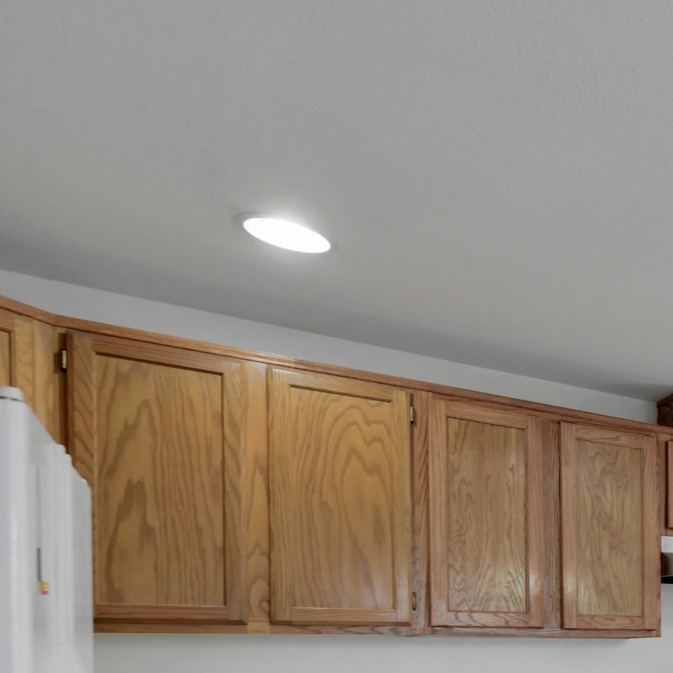 A round, recessed light fixture illuminates the ceiling, casting a soft glow in the room above the wooden cabinets.