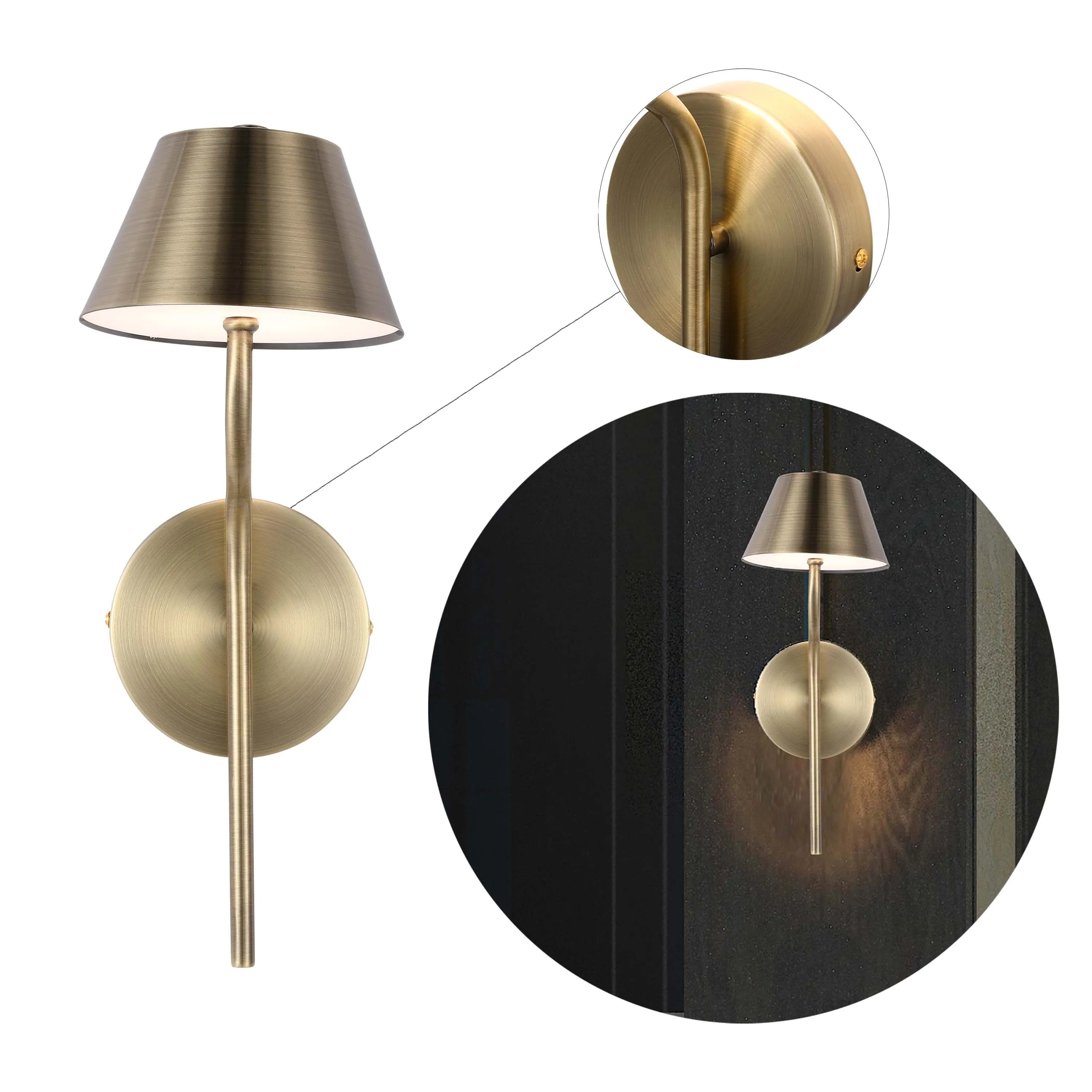 A bronze wall lamp with a conical shade, featuring a circular backplate and elongated arm. The lamp emits a soft, warm glow.