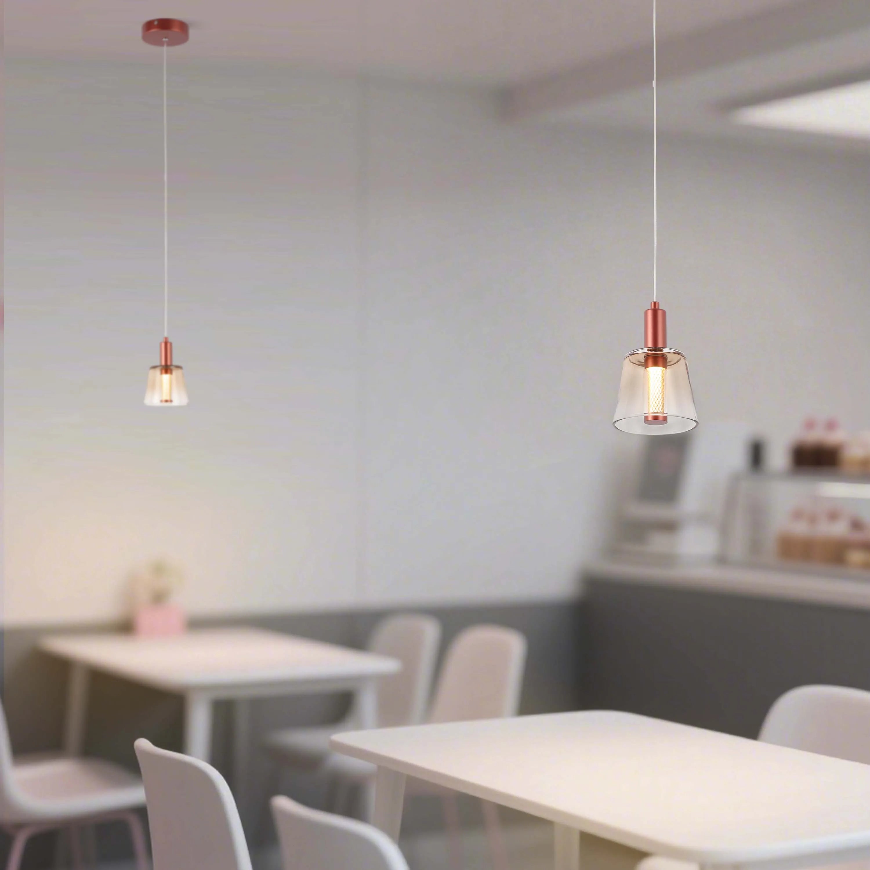 Two copper pendant lights illuminate a modern café interior. The lights have glass shades and hang above tables.