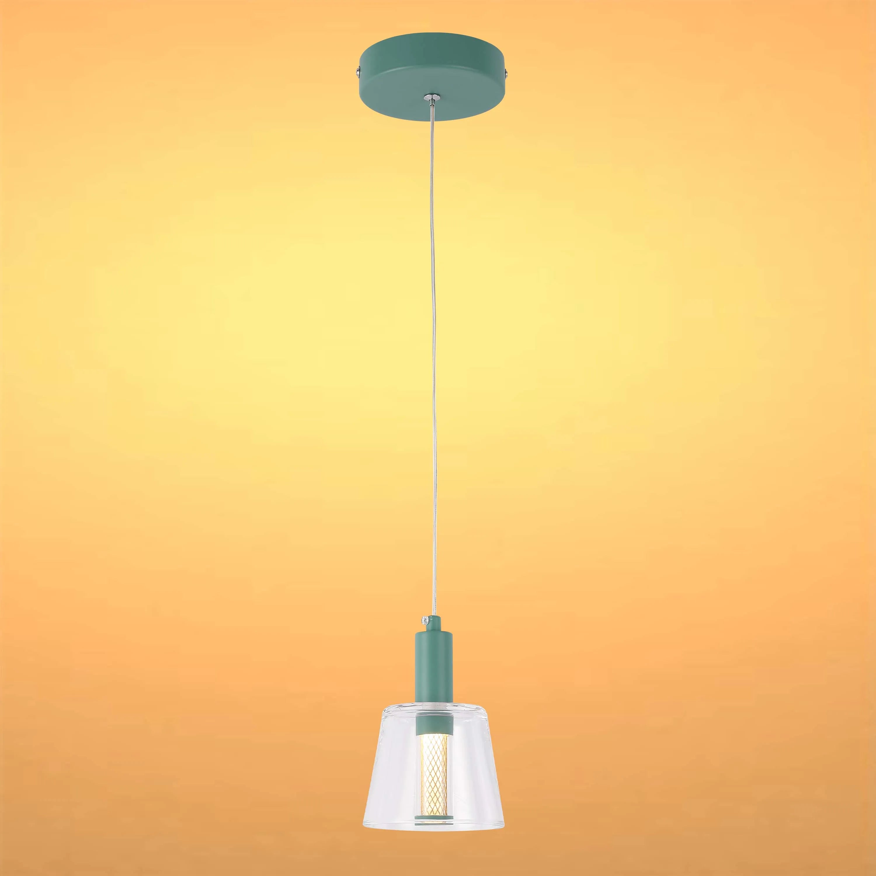 A hanging pendant light with a clear glass shade and a green mount against an orange background.