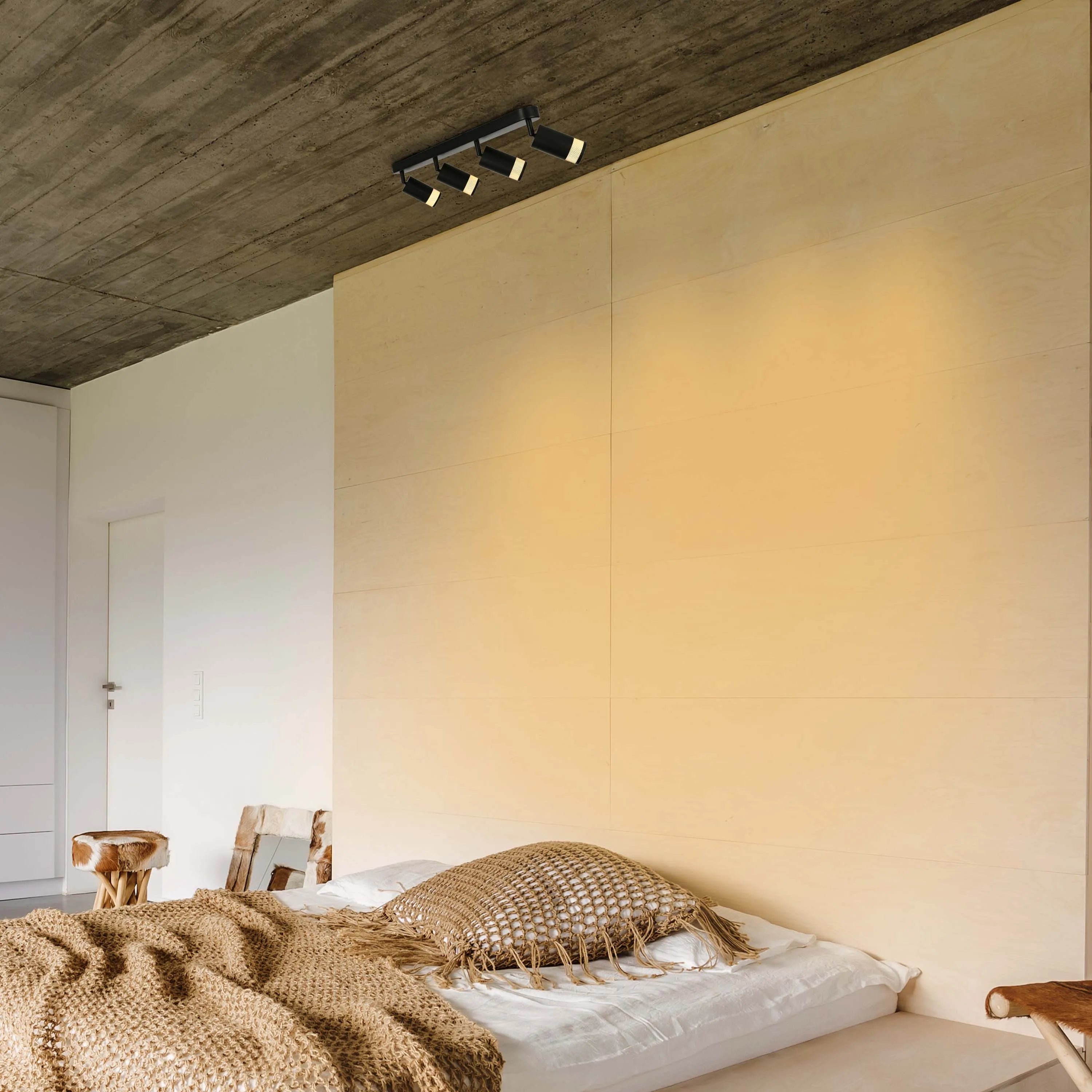 A black track lighting fixture with 4 spotlights illuminating a modern bedroom with warm light.