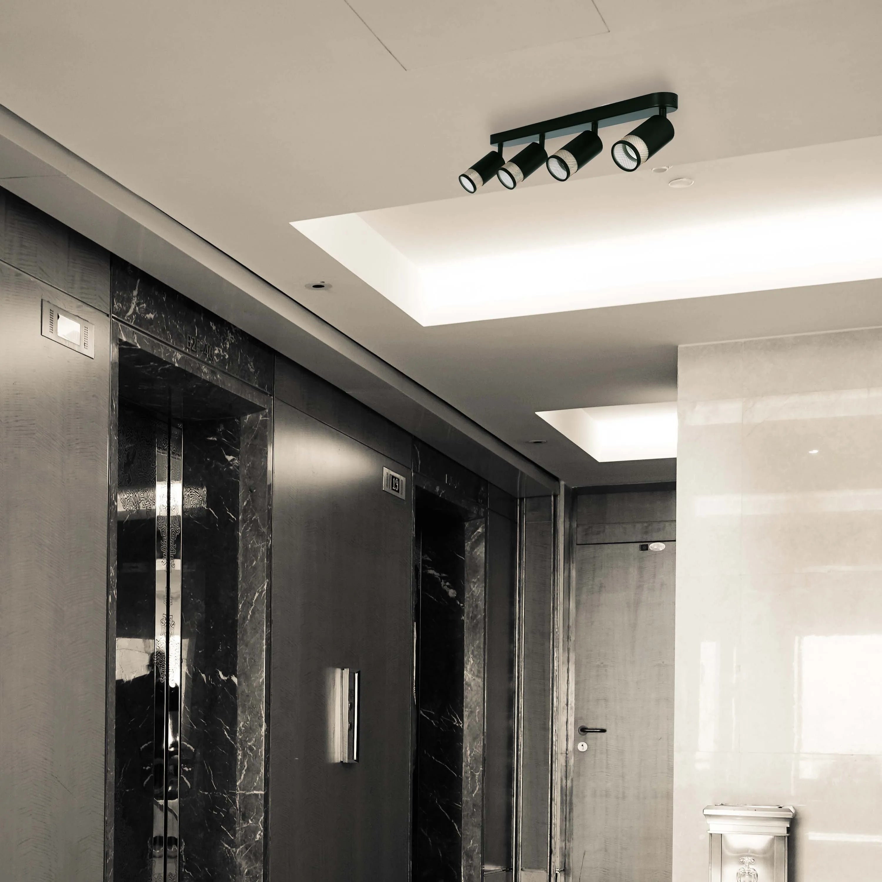 A modern, four-bulb track light fixture with cylindrical lamps provides focused illumination in an interior space.