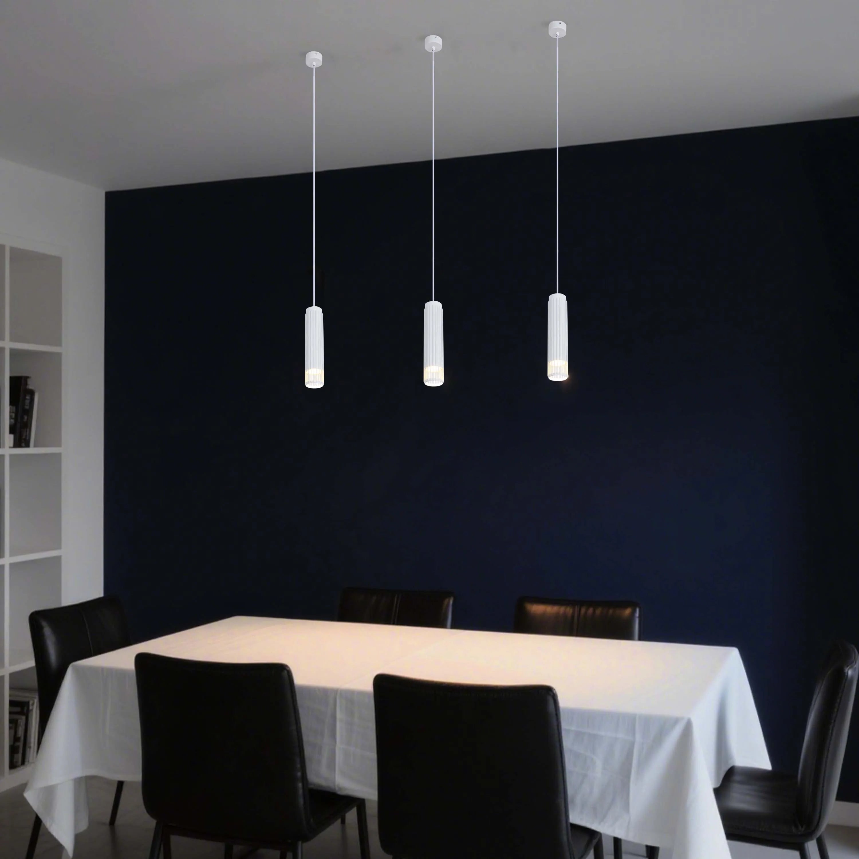 Three modern pendant lights hang over a dining table, each with a cylindrical white shade and emitting a warm, inviting glow.