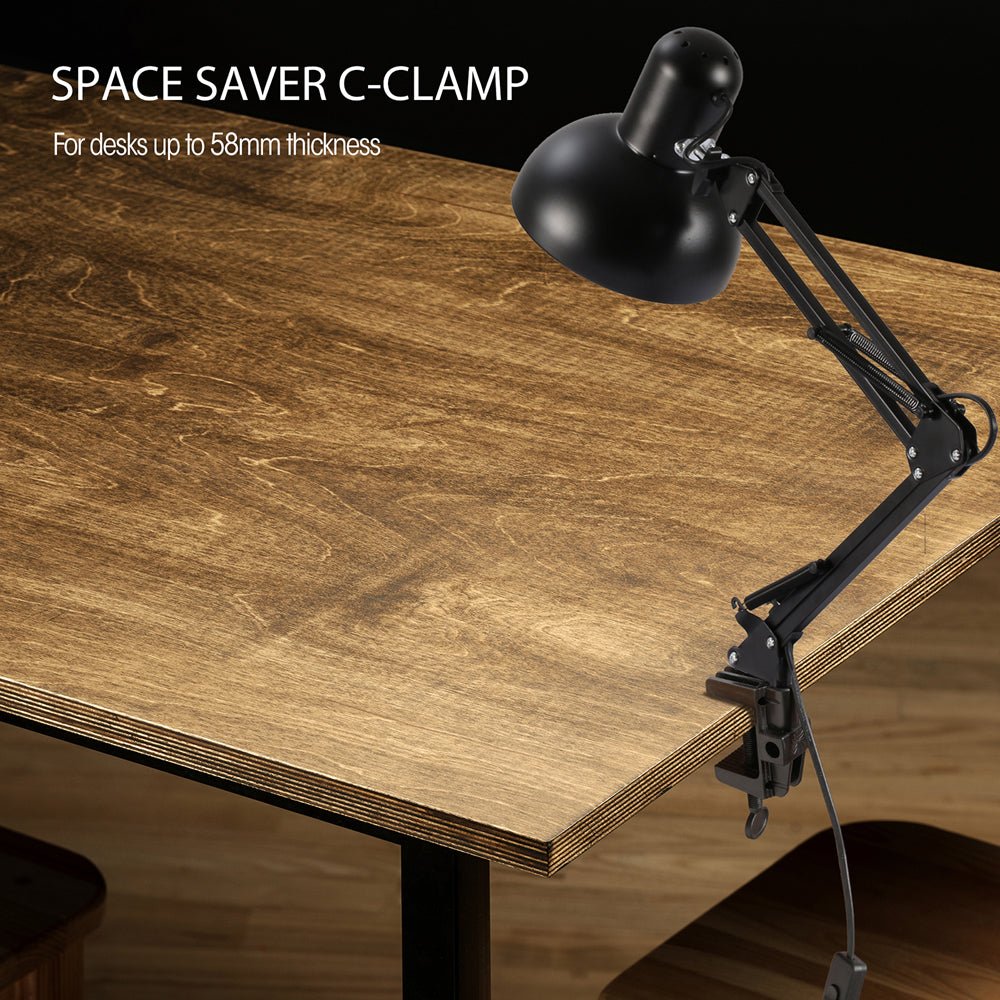 A desk lamp clamped to a wooden table, illustrating a space-saving design for a home or office.