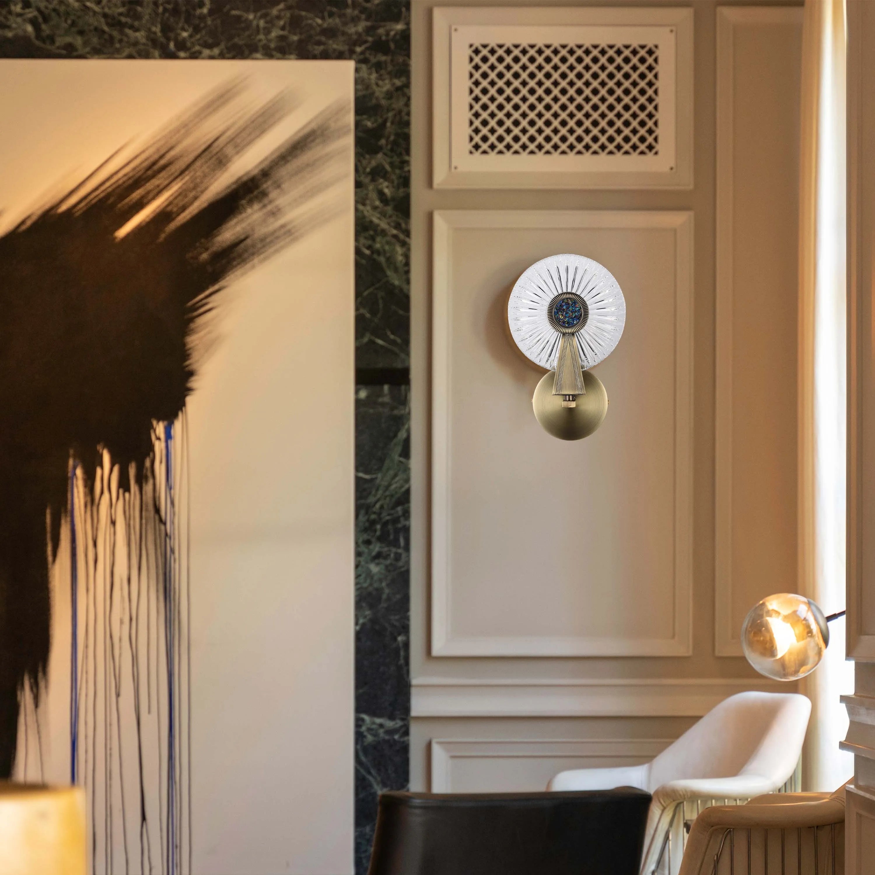 An ornate wall light in gold with a decorative glass shade, plus a glowing, suspended spherical light in the background.