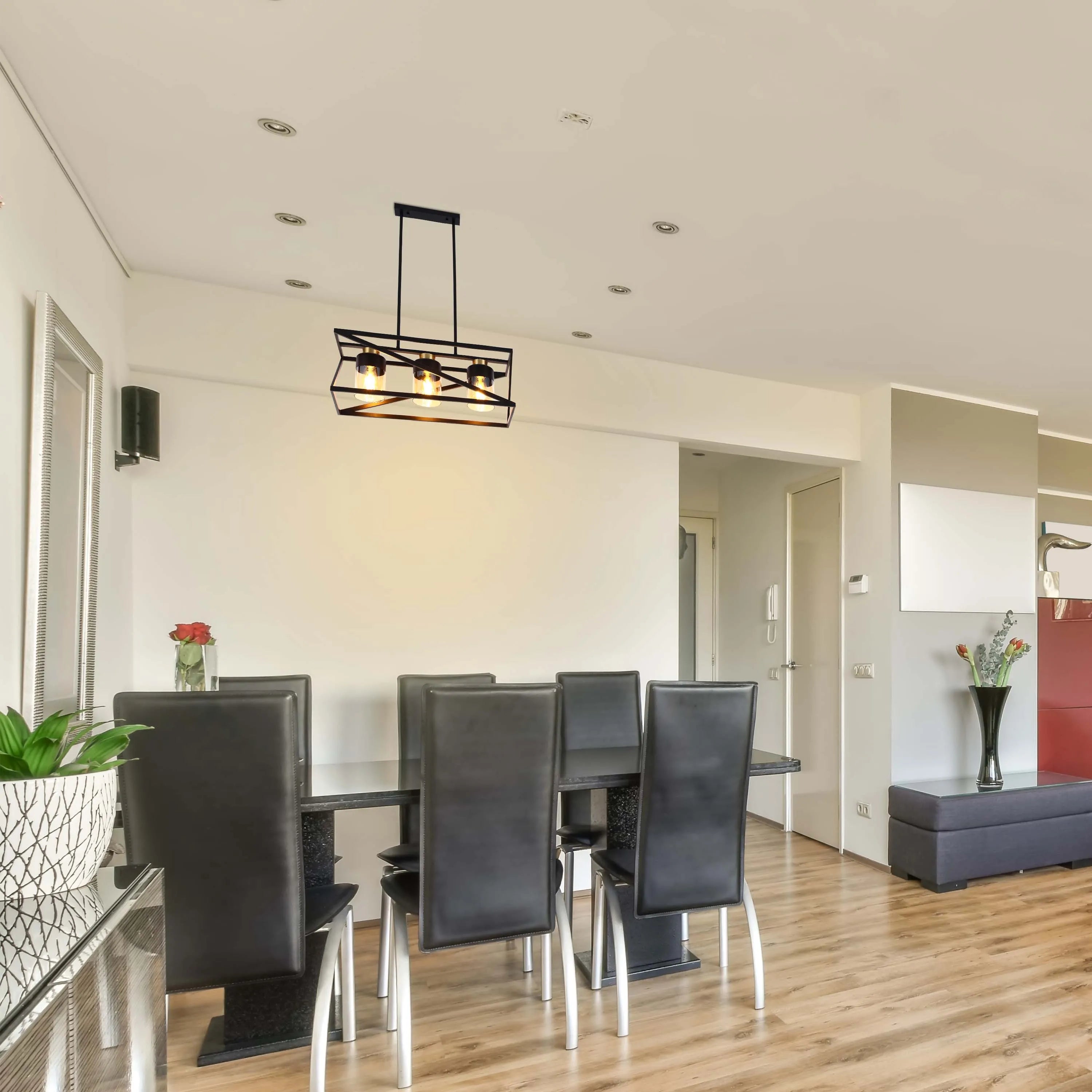 A modern chandelier hangs above a dining table, its warm glow contrasting with the sleek, dark chairs and minimalist decor.