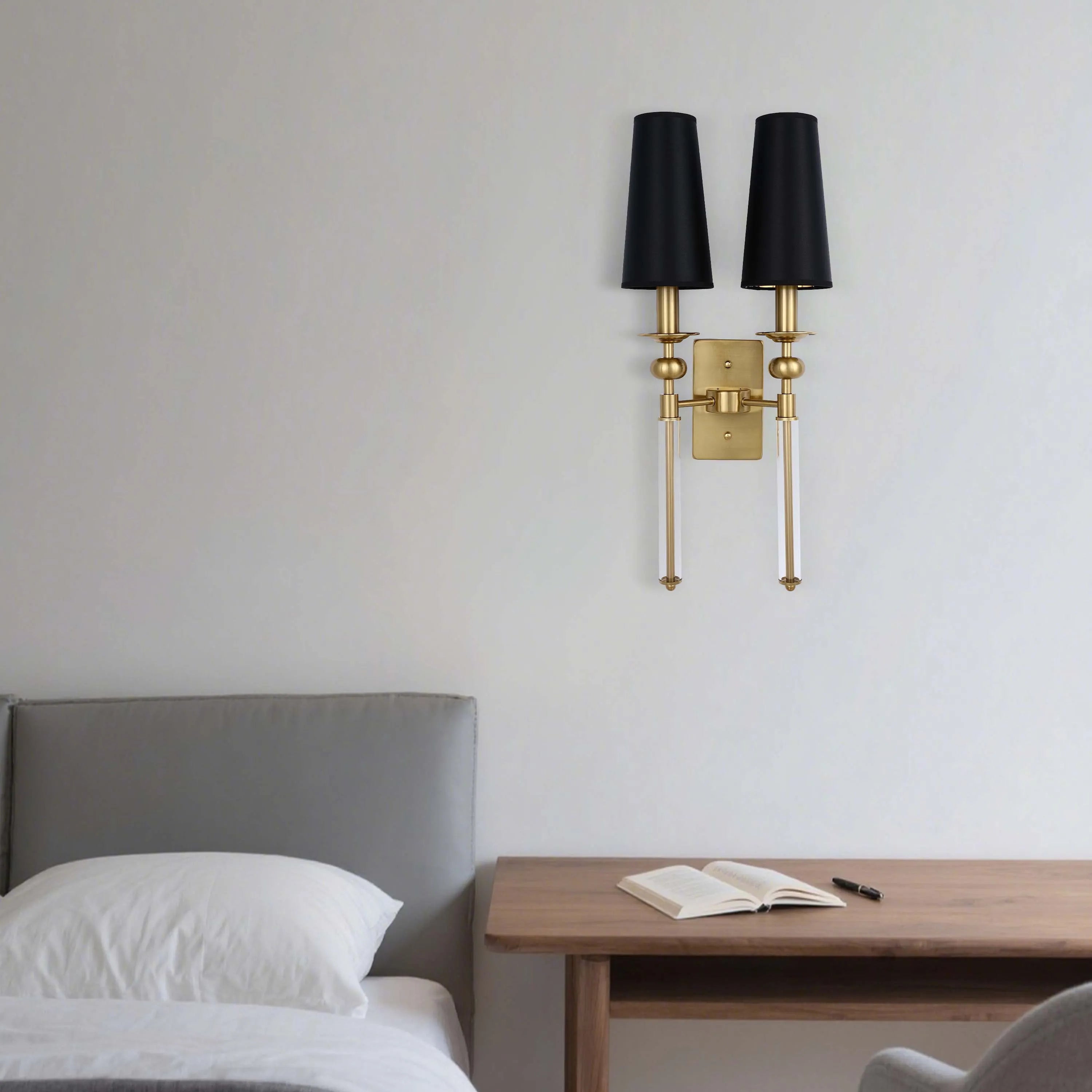 A gold sconce with two black shades, mounted on a light grey wall. Clear glass accents add a touch of elegance to this light fixture.