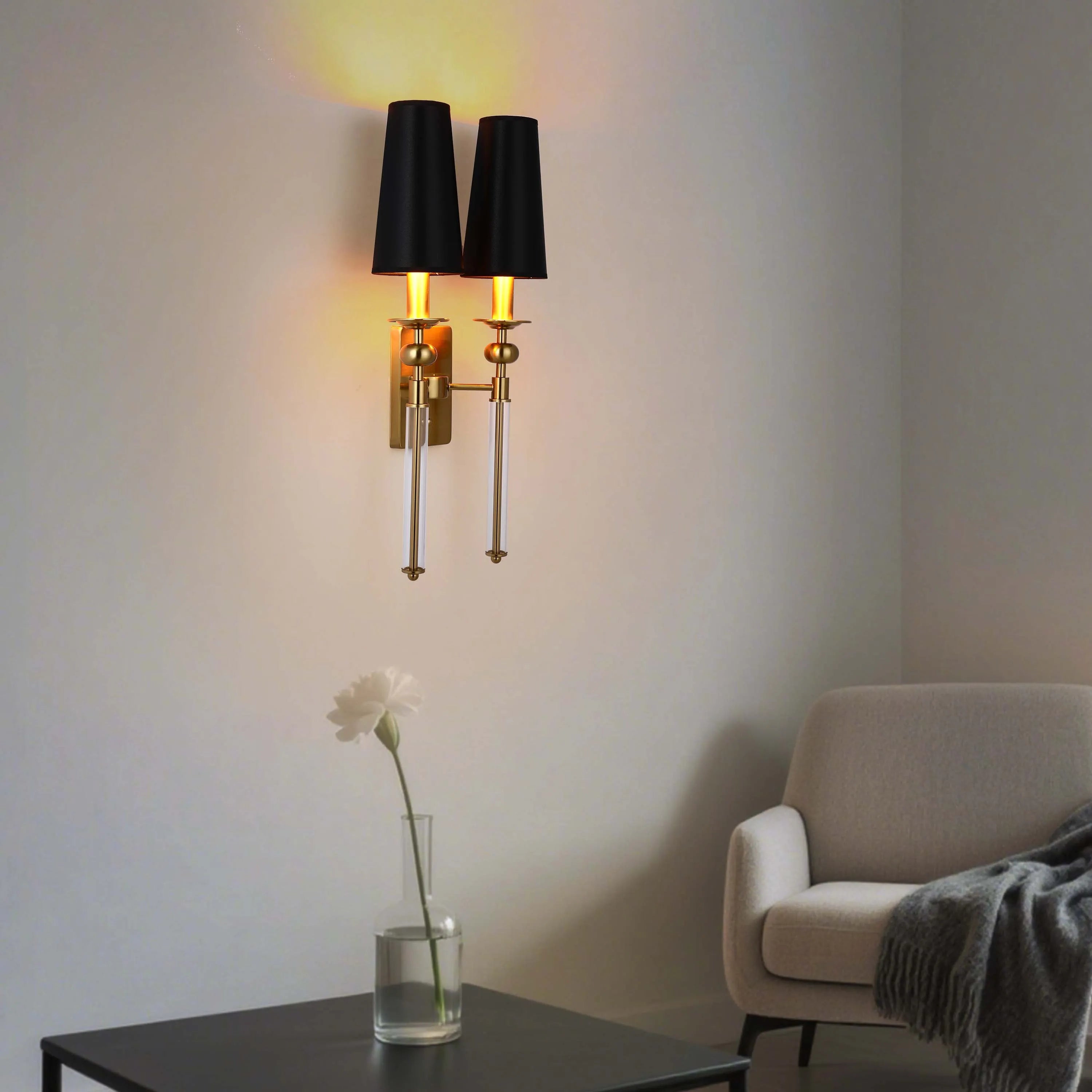 A pair of wall lights with black shades and gold hardware illuminate a modern living room. The warm glow of the bulbs adds a cosy touch.