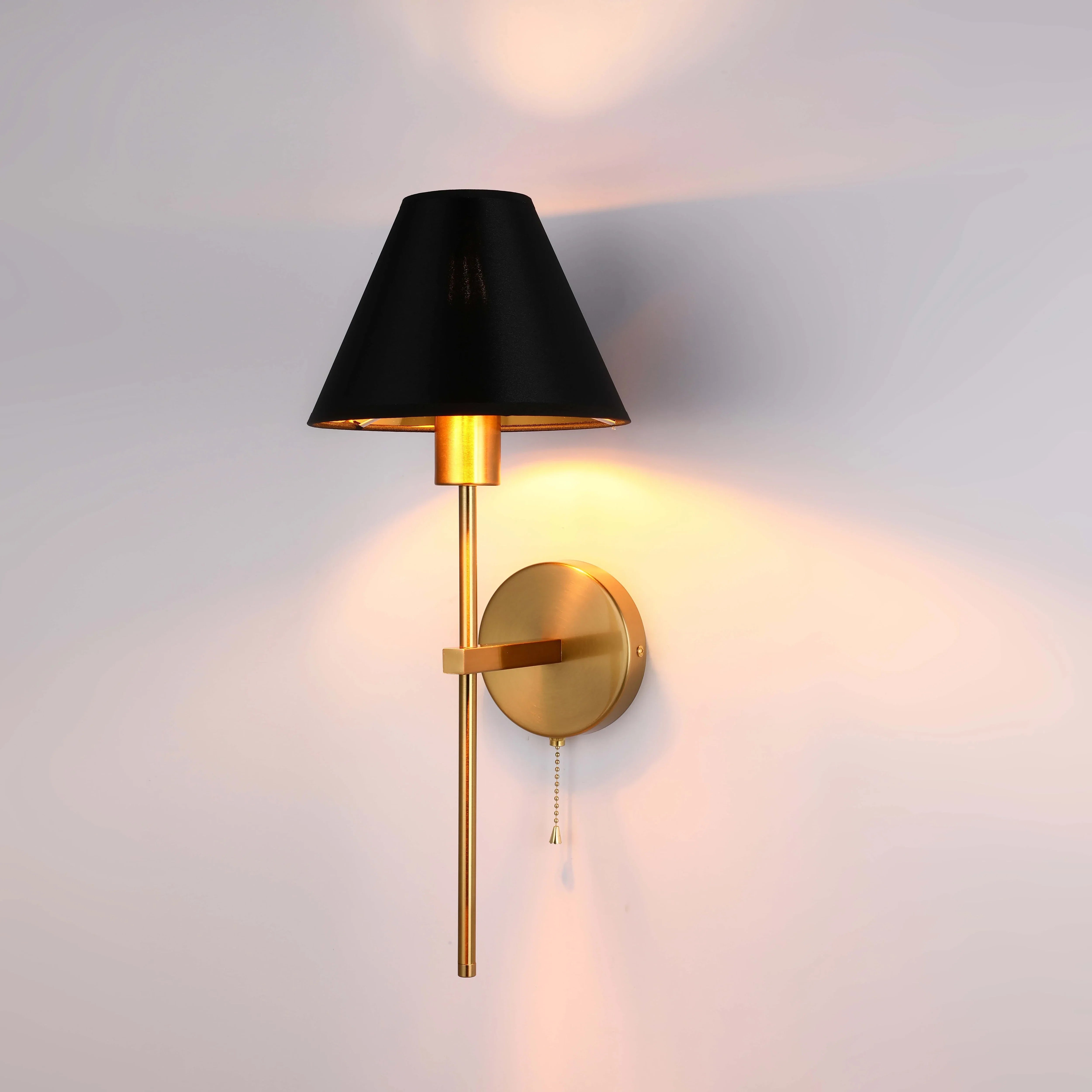 A stylish gold wall light with a black shade, emitting a warm, inviting glow on a neutral wall.