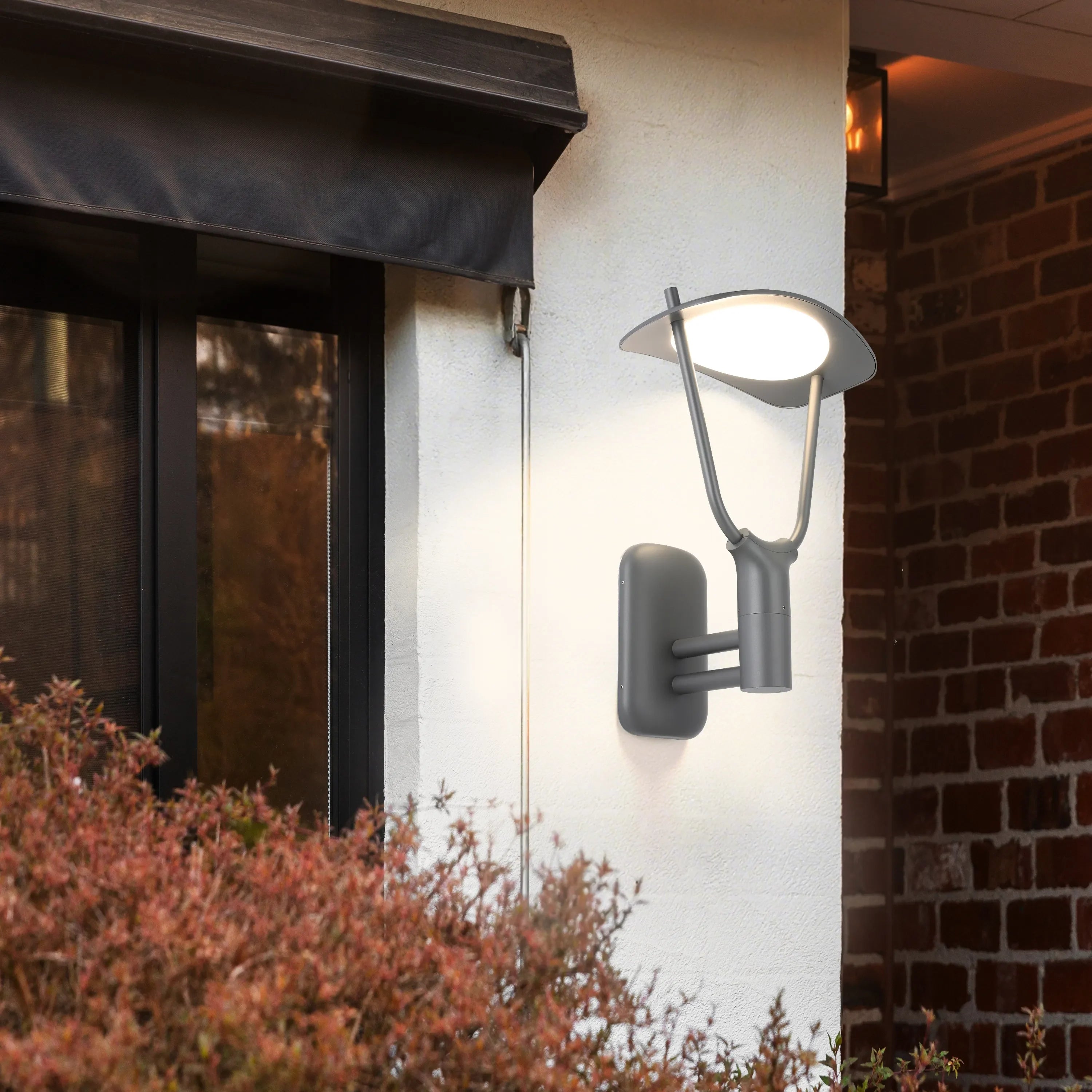 Contemporary outdoor wall light illuminating a building's exterior, casting a warm glow on the textured white wall and brickwork.
