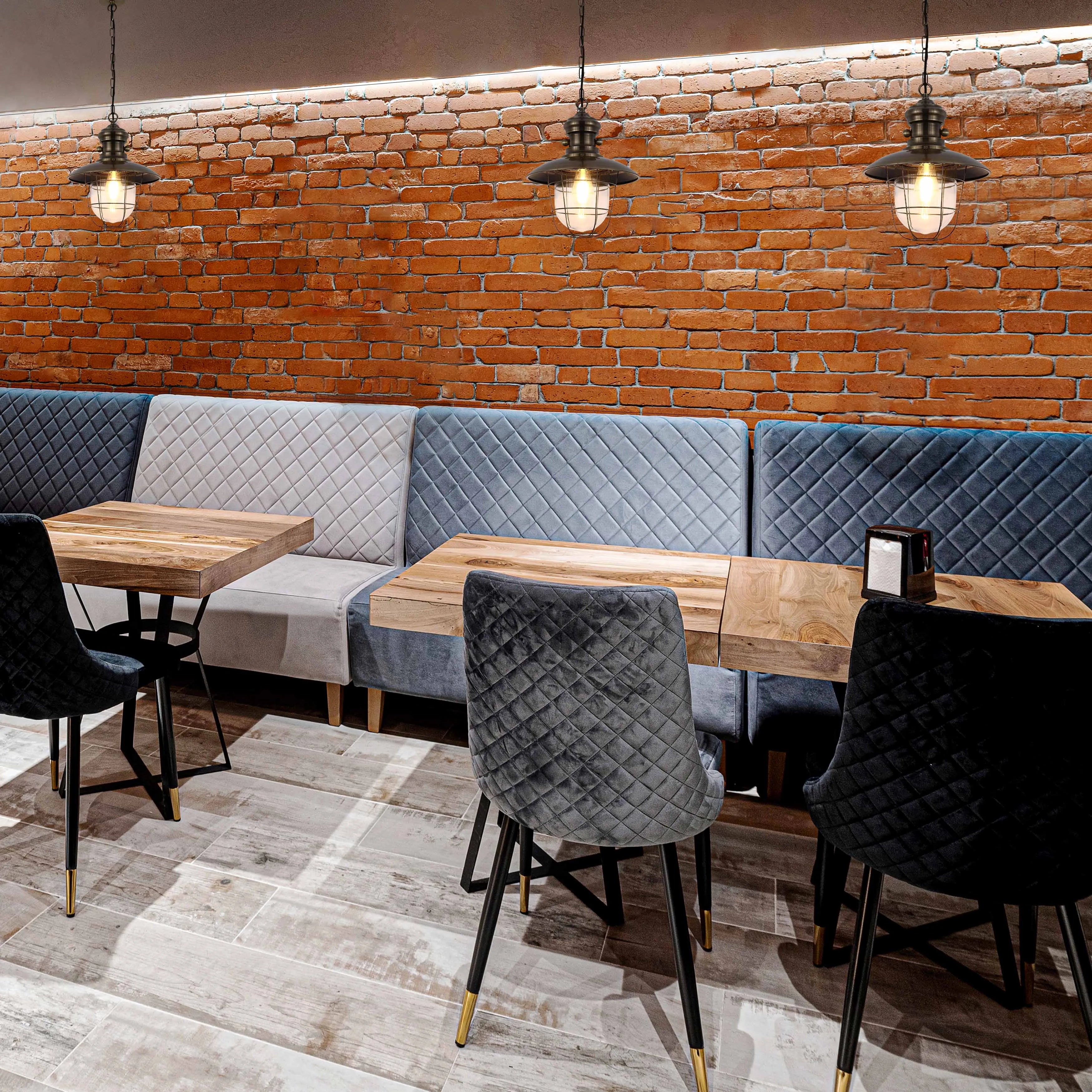 Rustic industrial pendant lights illuminate a cosy restaurant with exposed brick and plush quilted seating.