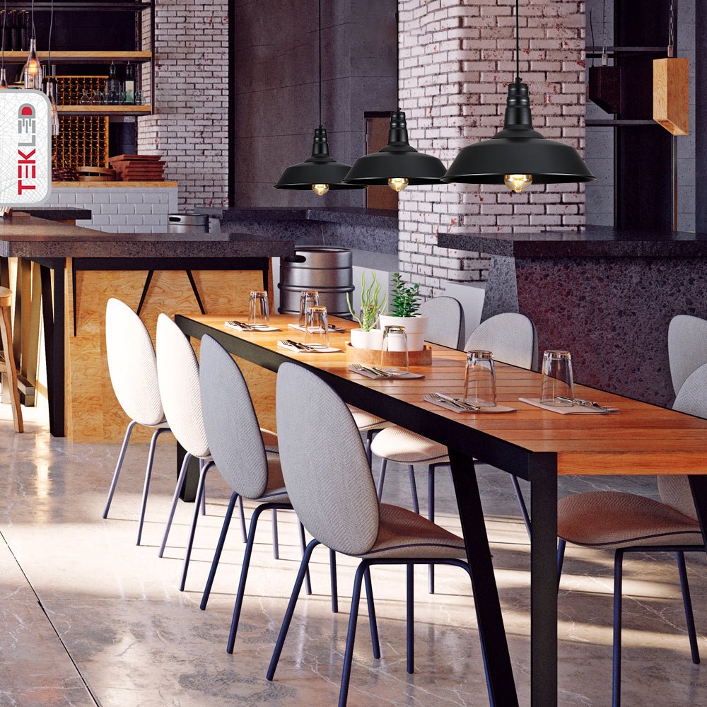 A dining area with a long, wooden table and fabric upholstered chairs beneath three black pendant lights.