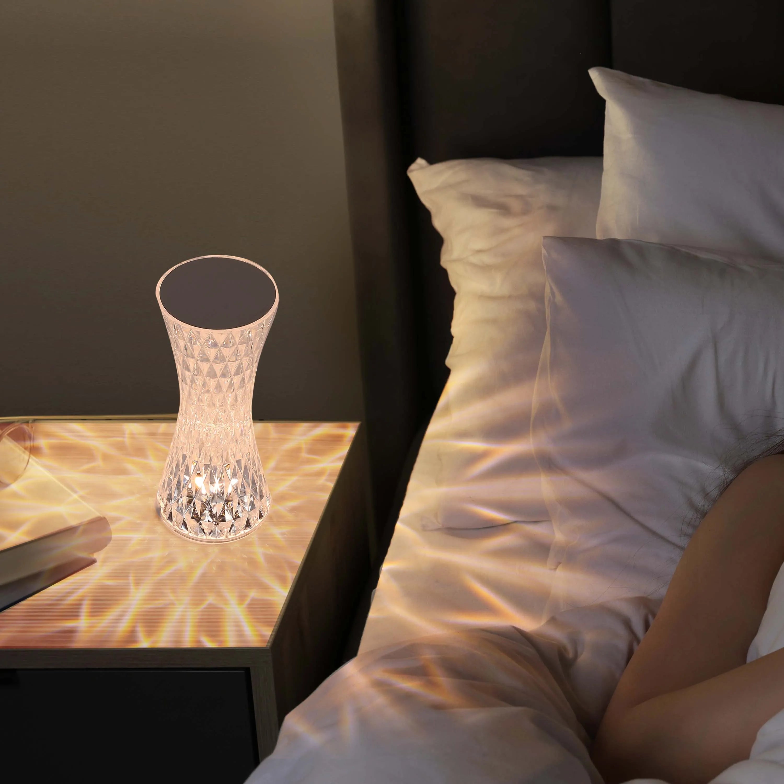 Bedroom lamp with a crystal-cut pattern casts a soft, warm glow onto the bedside table, creating a relaxing ambient light in the bedroom.