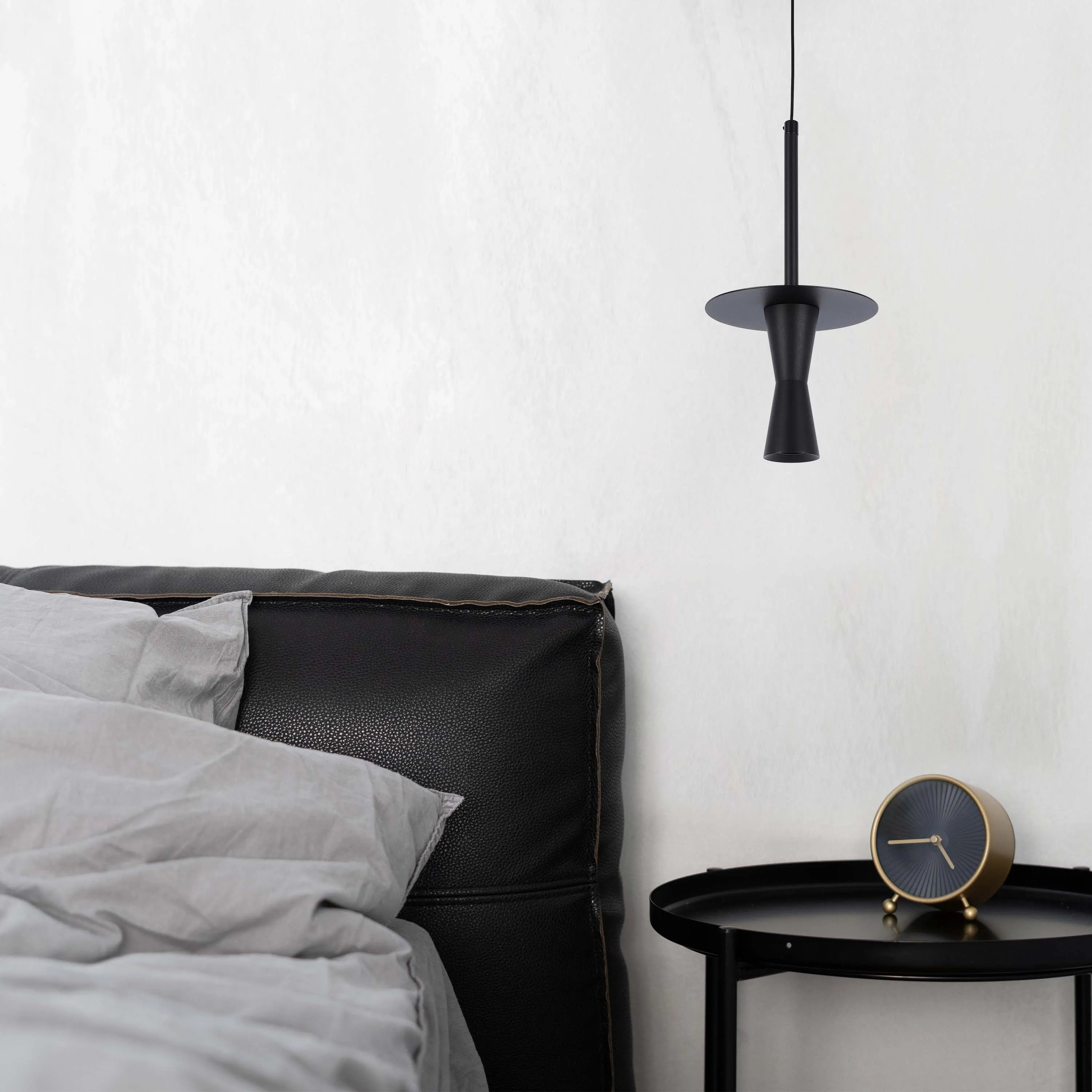 A modern, black pendant light hangs above a black side table and leather headboard in this stylish bedroom.