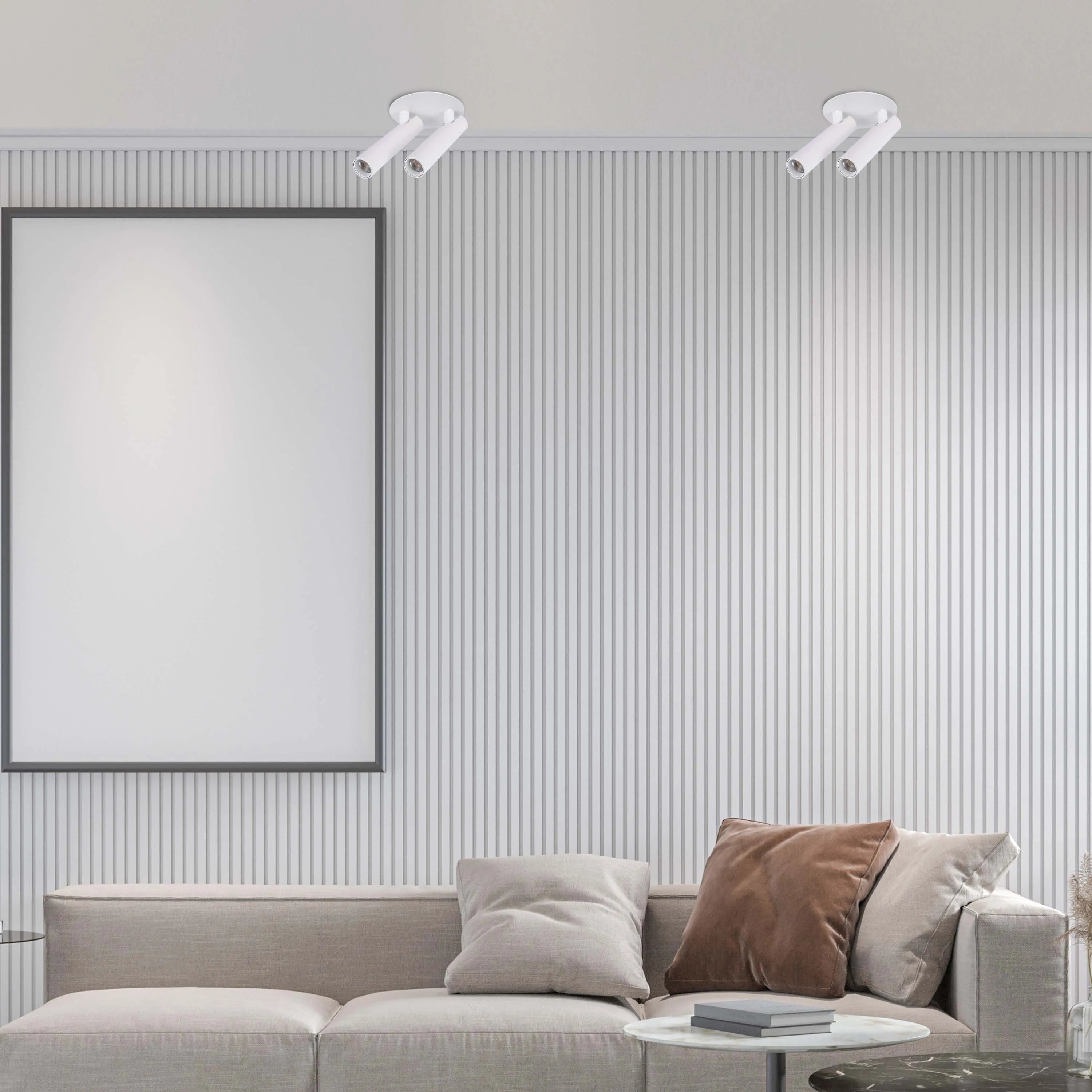 Minimalist white spotlights illuminate a living room with a blank framed poster above a modern sofa and side tables.