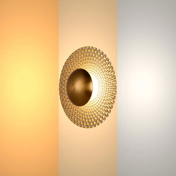 A gold wall light with a round, textured shade, evenly lit with a soft, diffused glow.