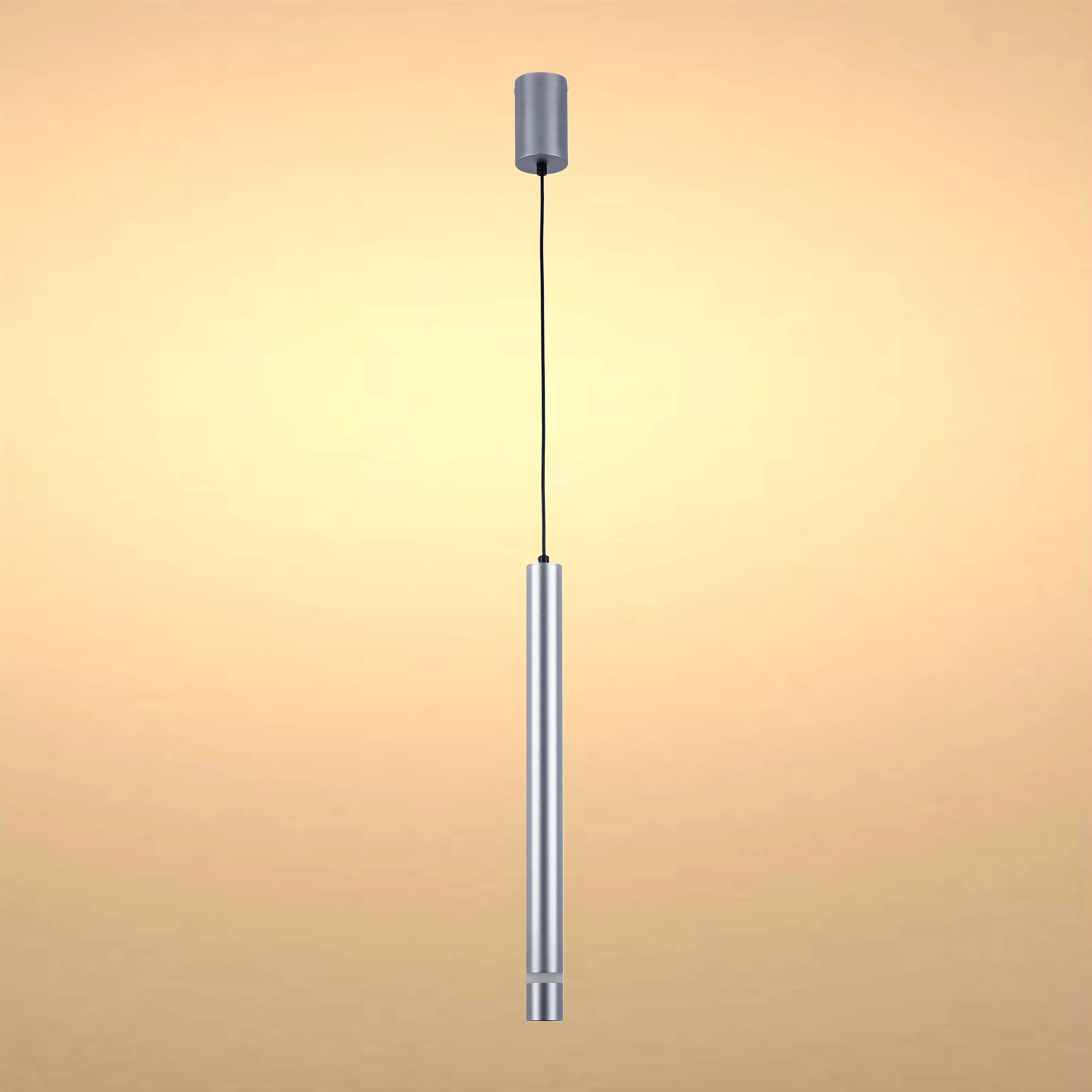 A cylindrical, silver pendant light hangs from a black cable, softly lit against a warm, neutral background.