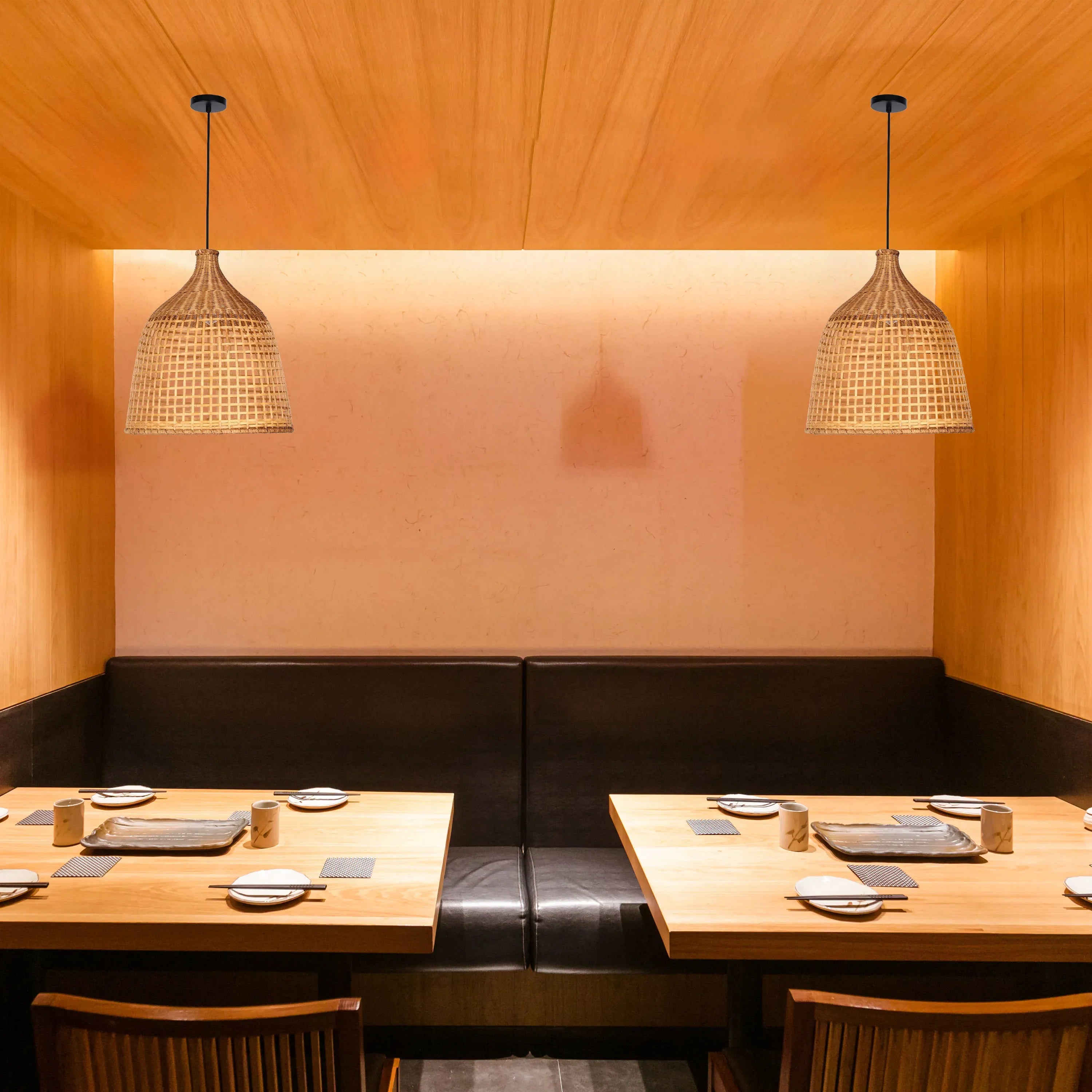 Two pendant lights with woven shades illuminate a restaurant booth with wooden tables, black leather seating and warm, inviting ambiance.