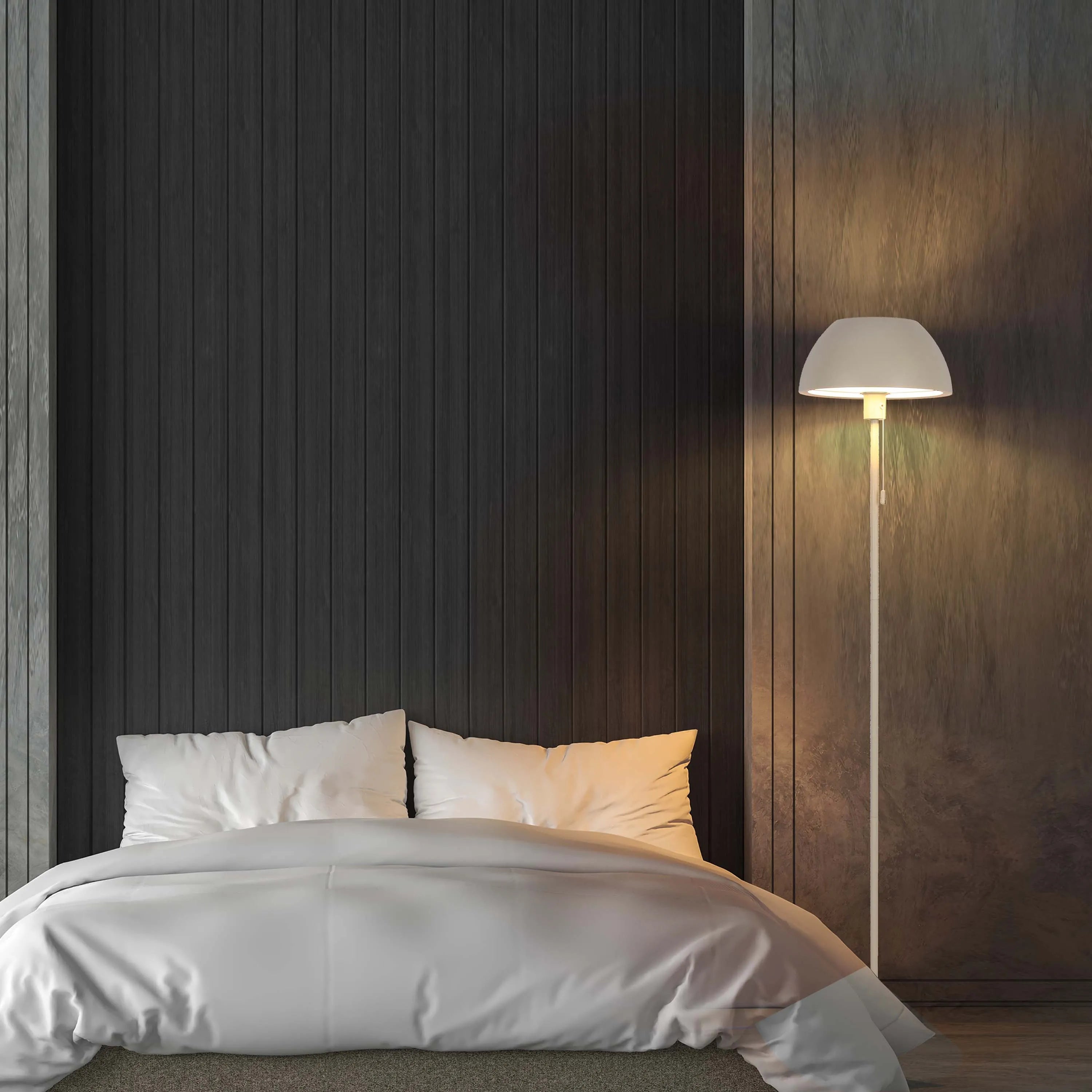 Warm ambient light from a white floor lamp illuminates a modern bedroom with dark wood panelled walls and a bed with white linen.