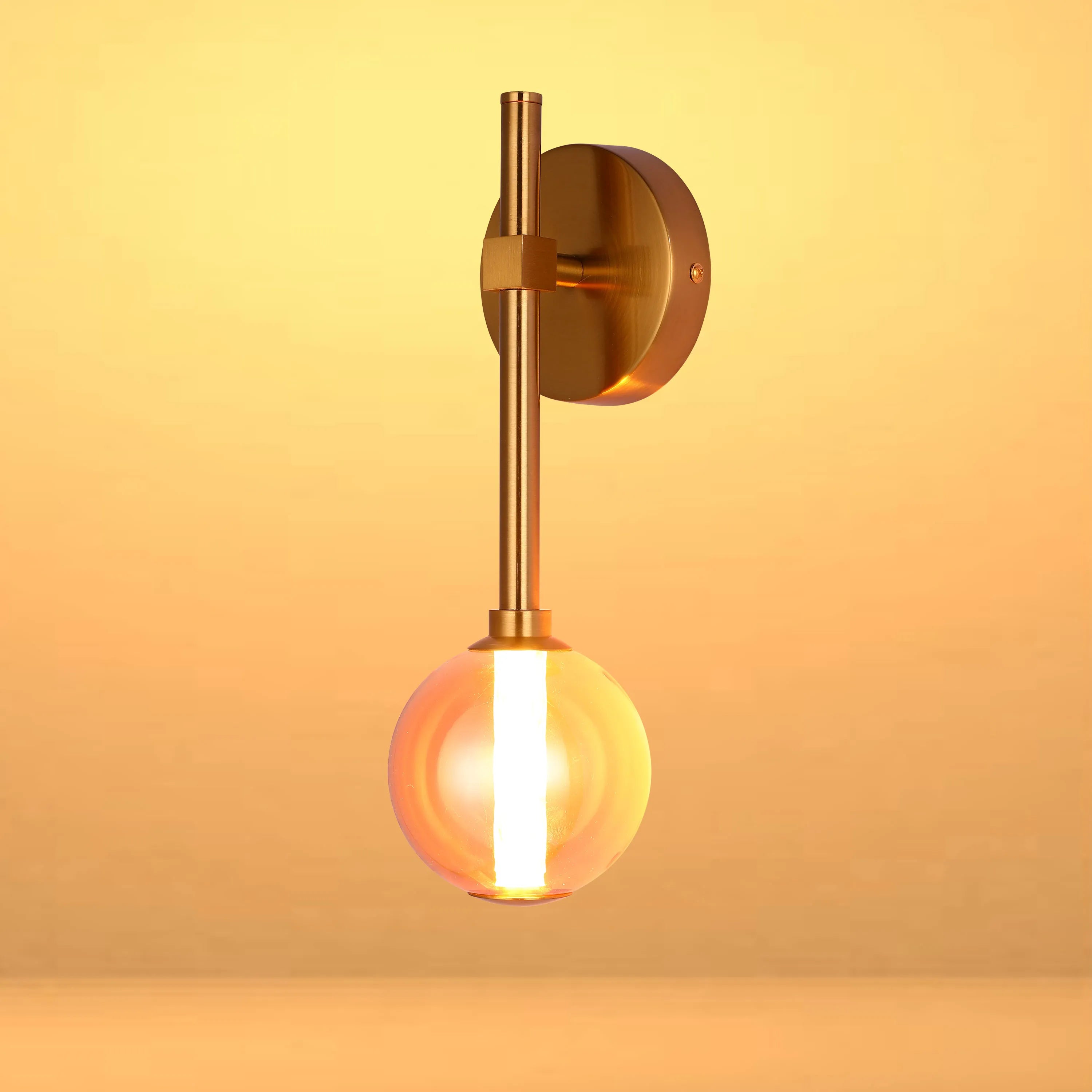 A modern wall light with a brass finish and a spherical glass shade, emitting a warm, ambient glow.