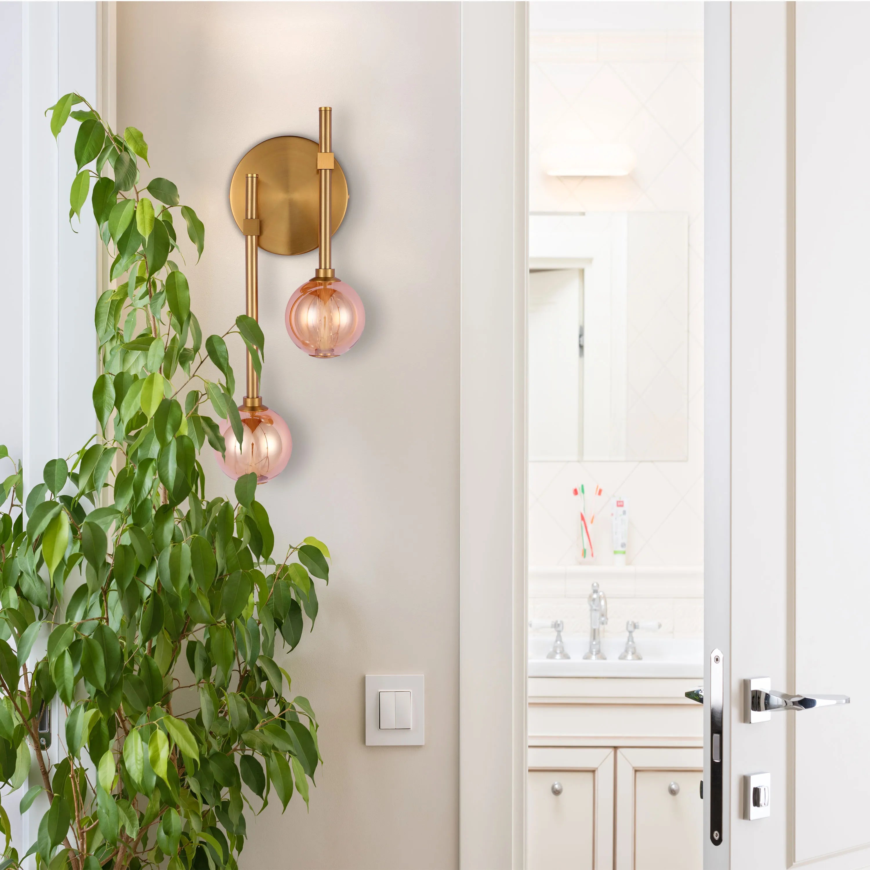 A stylish wall light with a brass finish and two pink glass globes, creating a warm and inviting atmosphere.