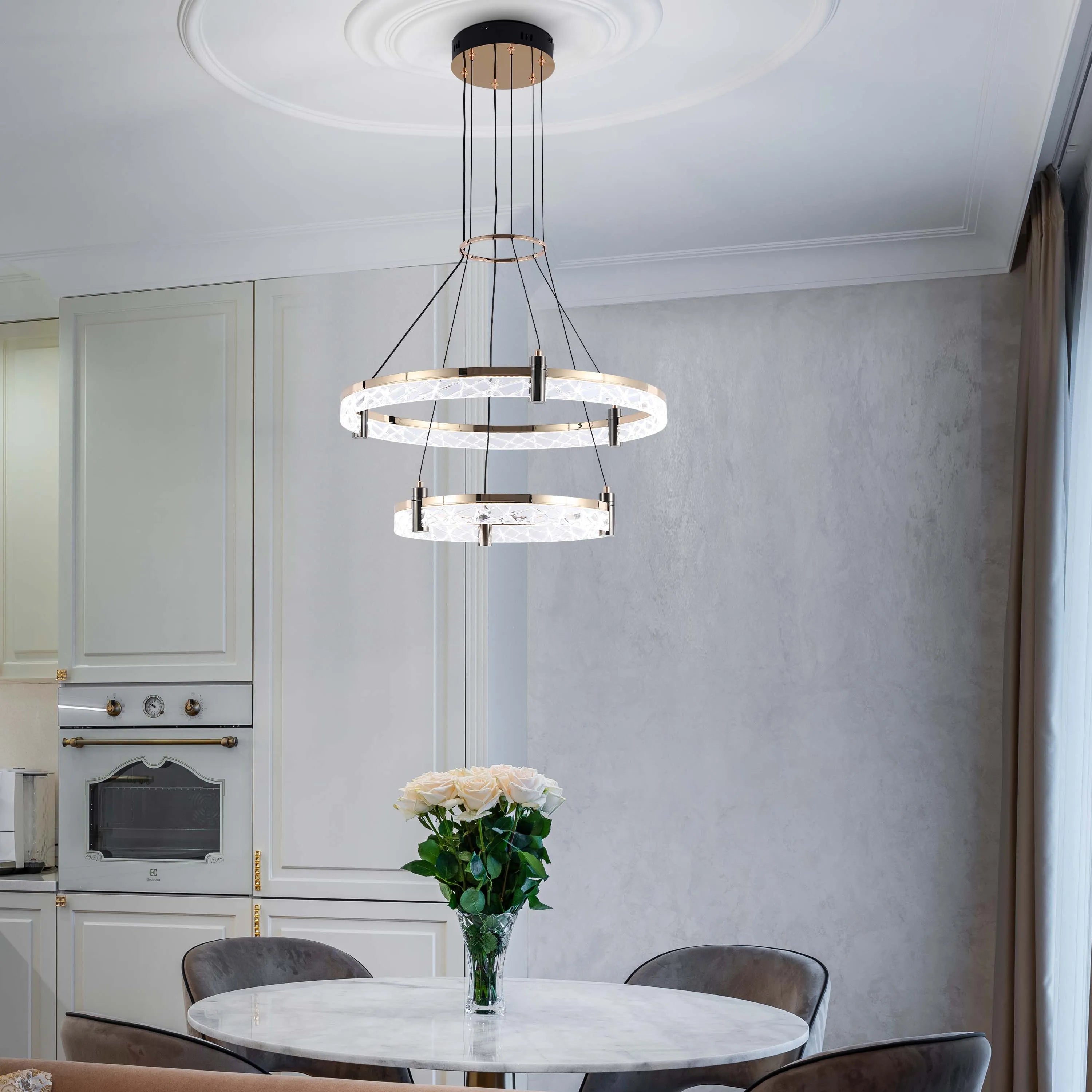 A luxurious two-tiered circular chandelier hangs above a marble dining table in a modern, elegant kitchen.