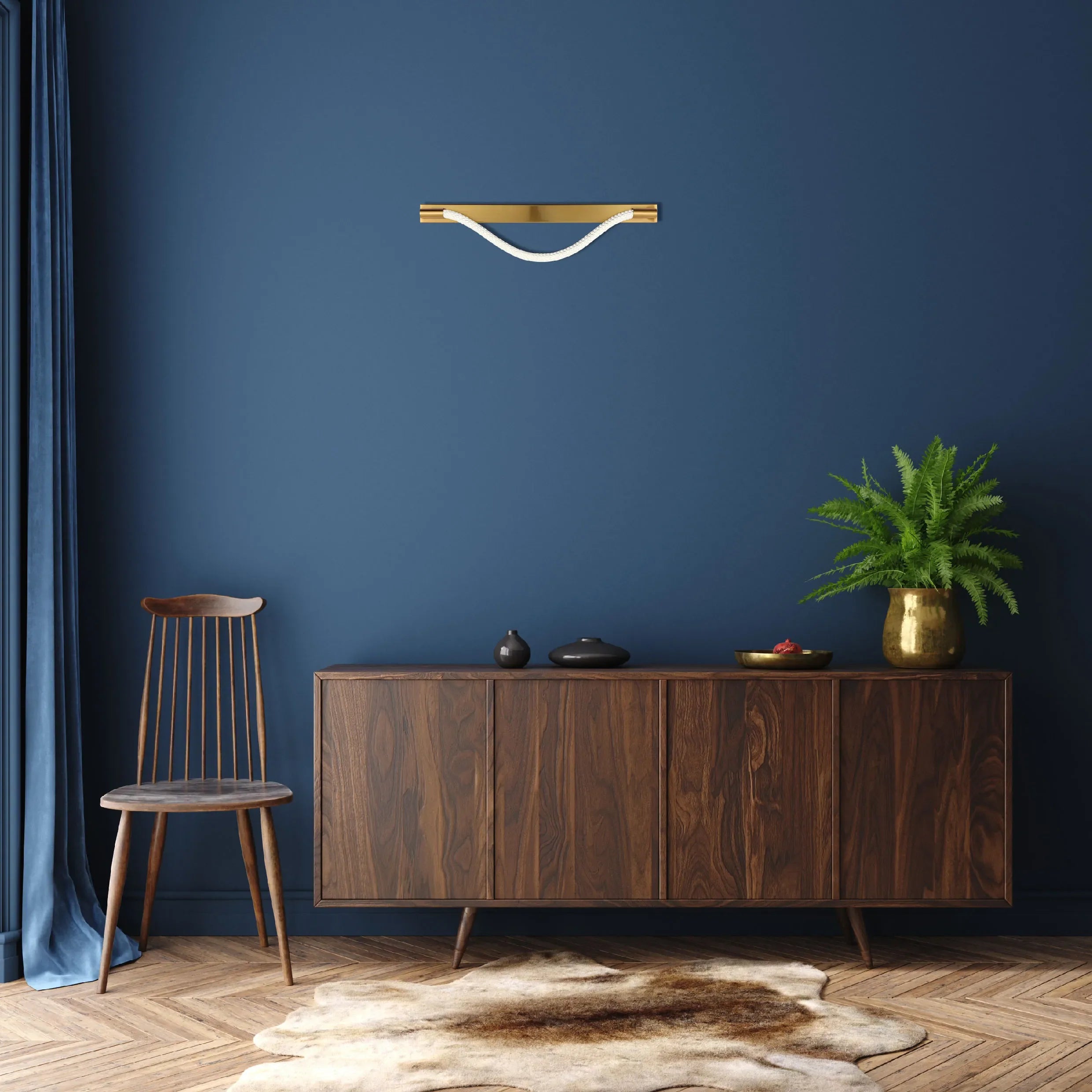 A warm, modern wall light with a gold fixture and a white rope detail, set against a dark blue wall, casting a soft glow.