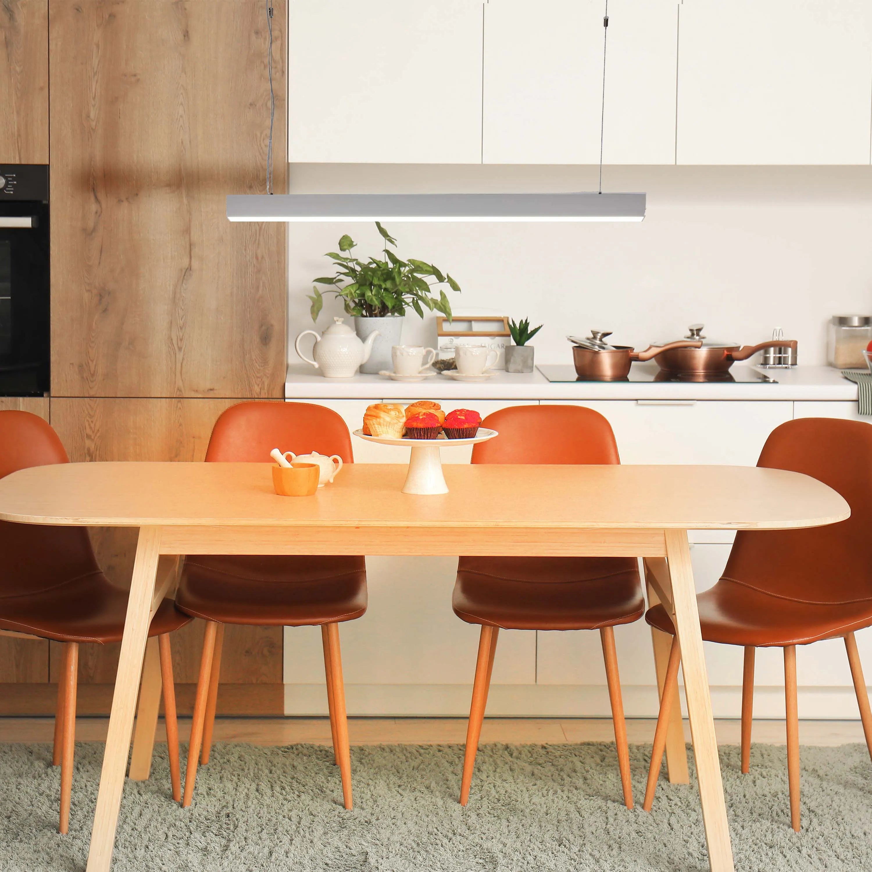 Contemporary dining area featuring a linear pendant light over a wooden table with brown leather chairs.