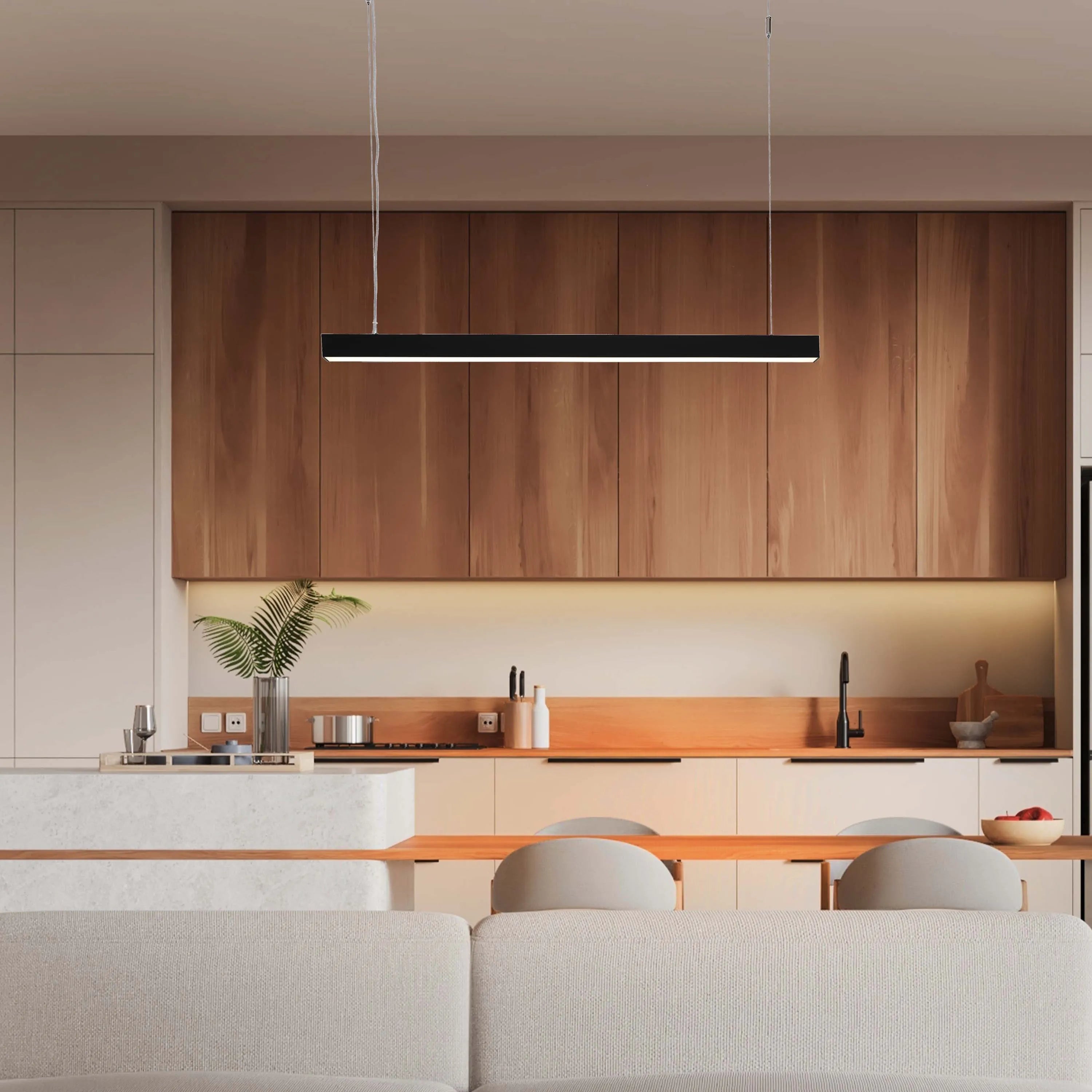 A modern kitchen features a sleek, linear LED pendant light, suspended over a dining area. The warm glow complements the wood cabinetry.