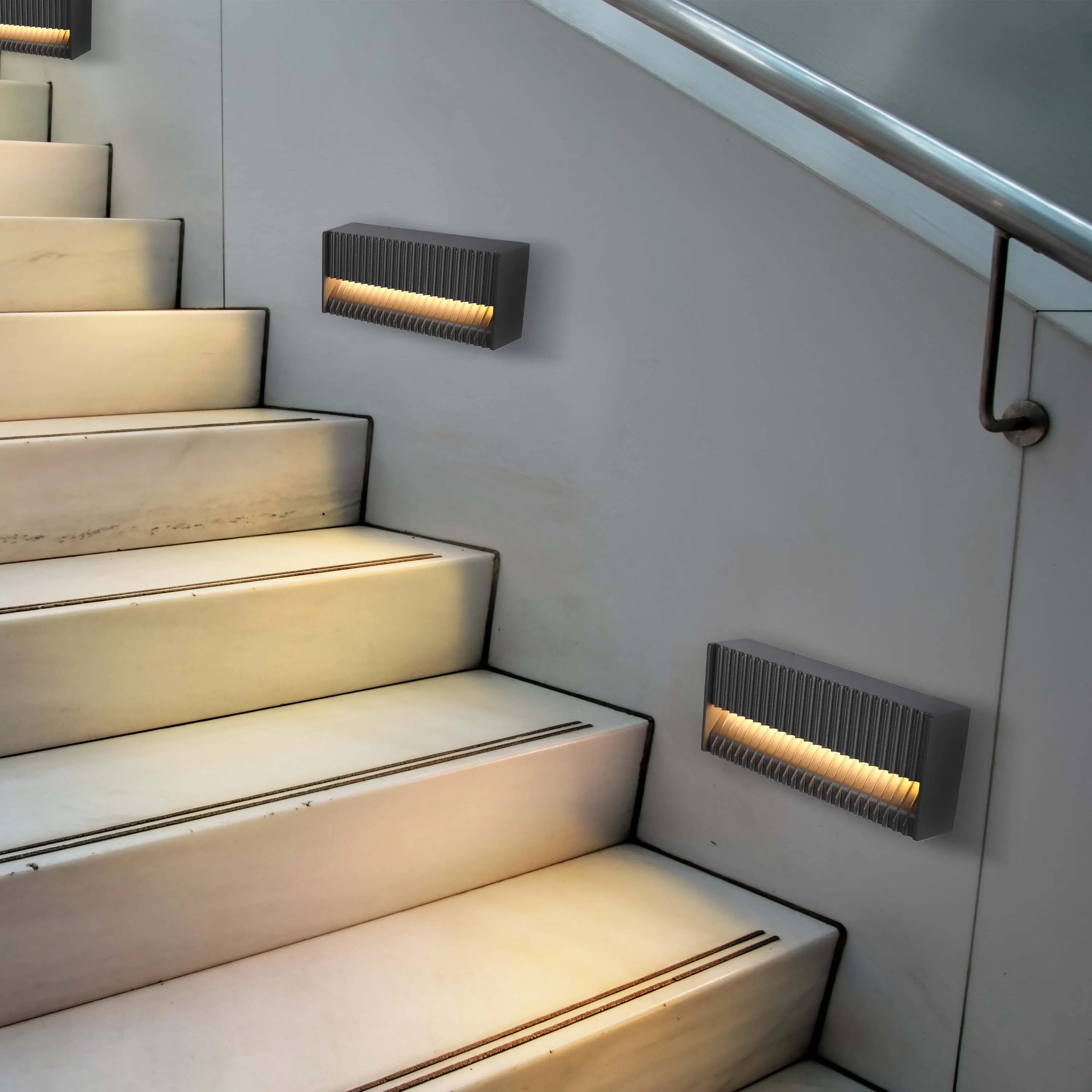 Stairway with modern, slatted wall lights, casting a warm glow onto marble steps. Handrail in view.