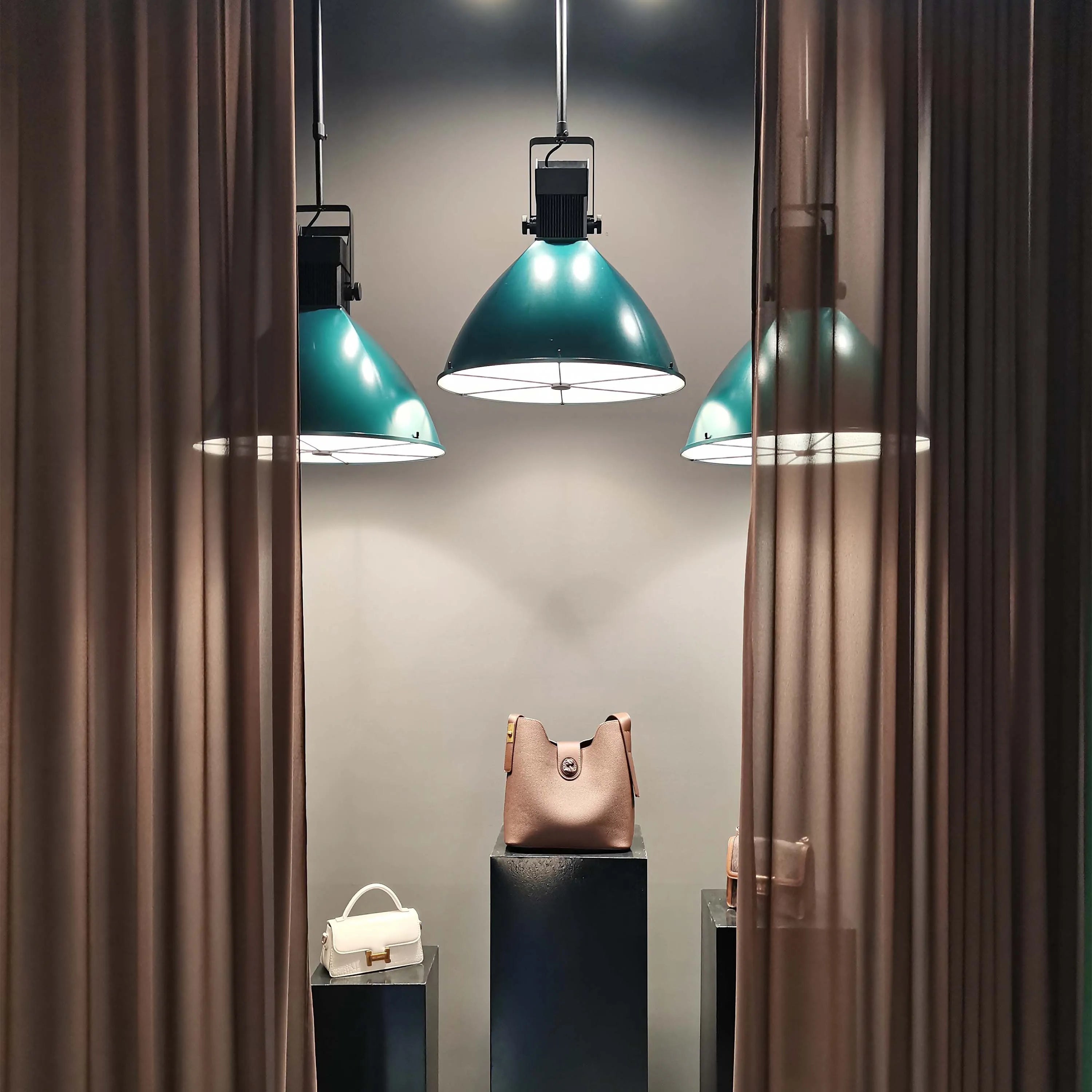 Stylish teal pendant lights with a contemporary, industrial design illuminate handbags in this display. A chic and modern statement piece.