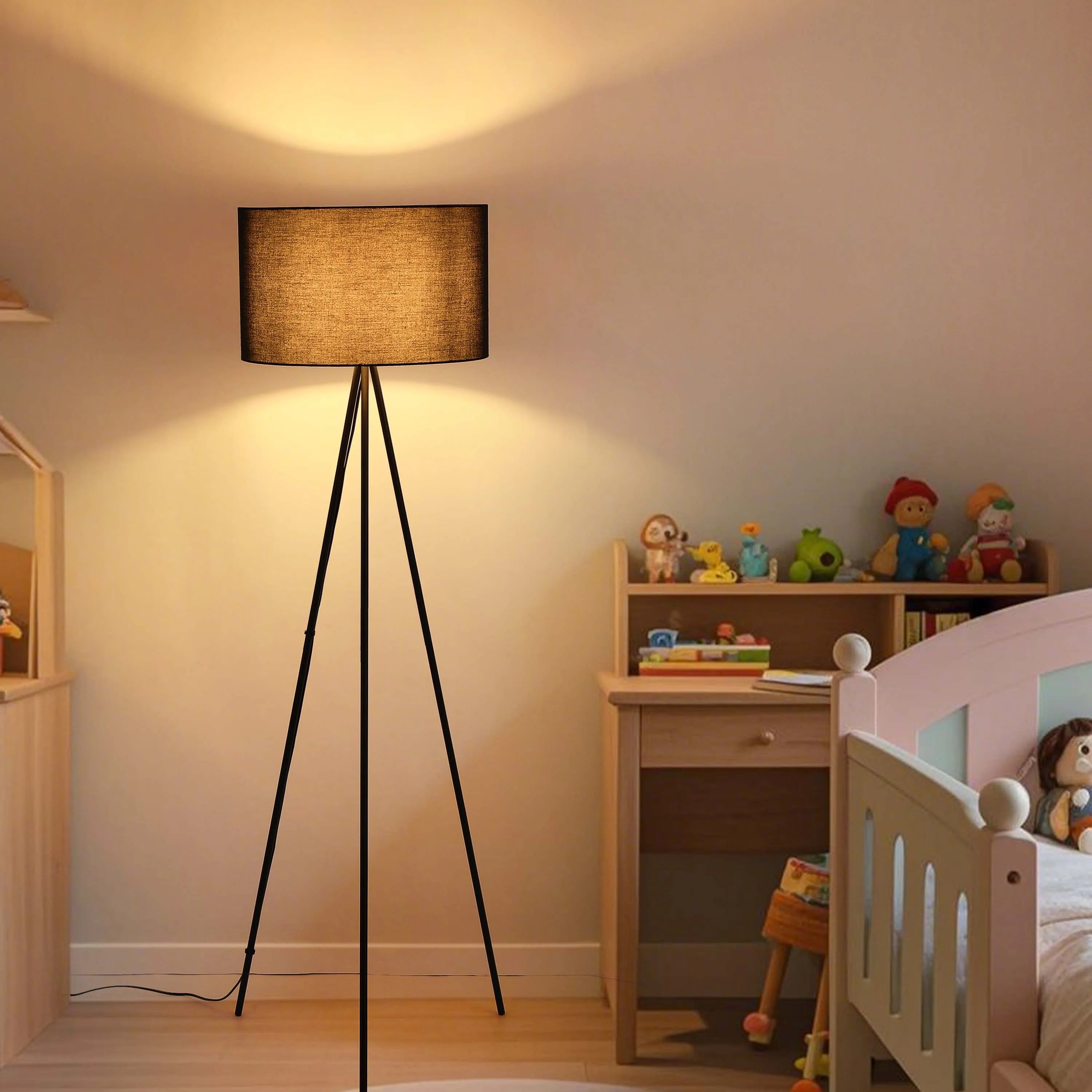 A floor lamp with a tan shade casts a warm glow in a cosy, child's bedroom. The lamp has a black, tripod base.