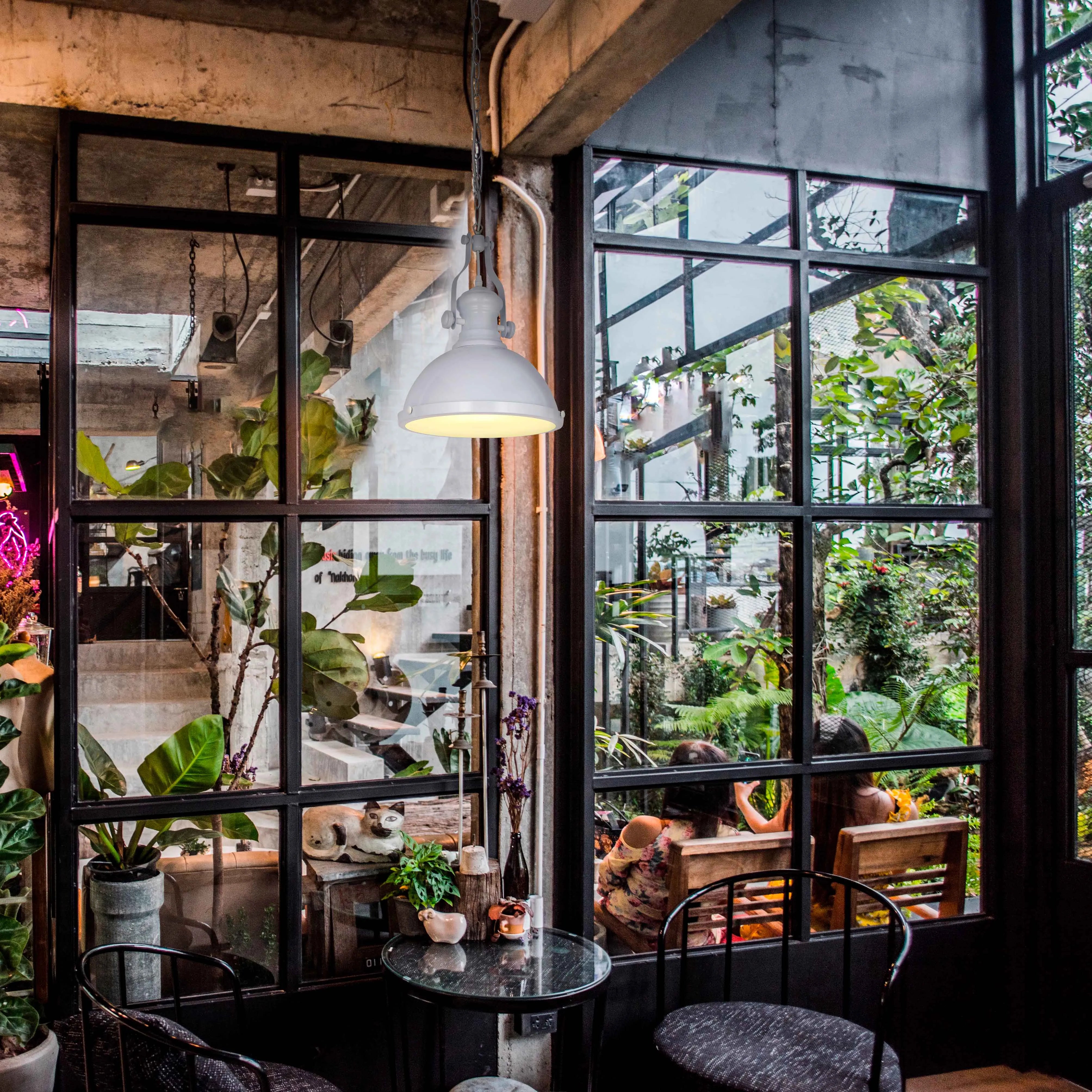 An industrial-style pendant light shines brightly, illuminating a cosy cafe interior with large windows and lush greenery outside.