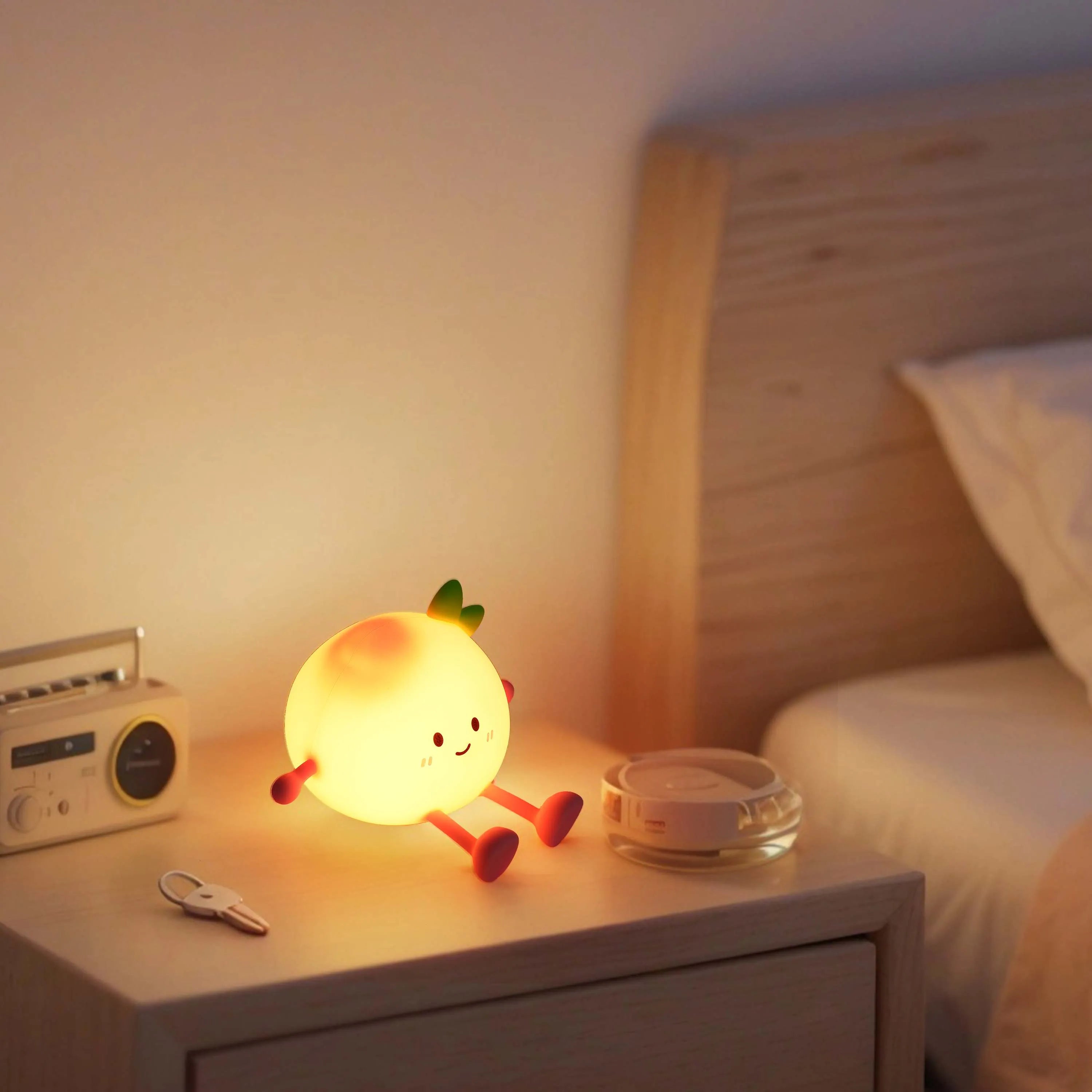Cute, warm-toned night light shaped like an orange sits on a bedside table. It creates a soft glow, perfect for a cosy atmosphere.