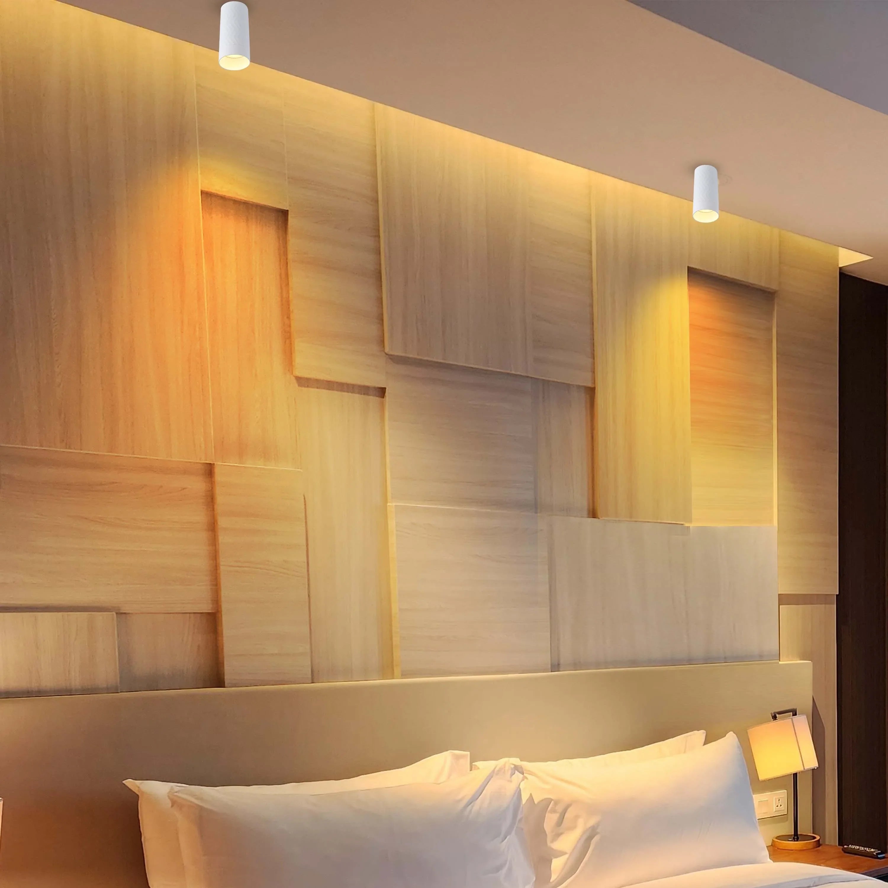 Modern bedroom lighting featuring cylindrical spotlights and a bedside lamp. The wooden wall adds a warm ambiance.