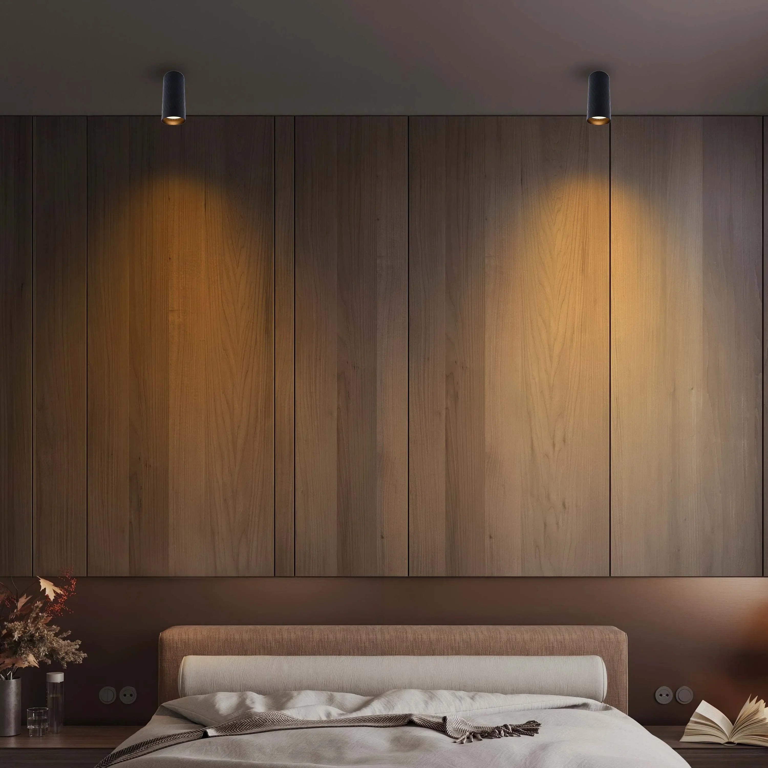A bedroom with two ceiling-mounted spotlights, casting a warm glow on the wooden headboard.