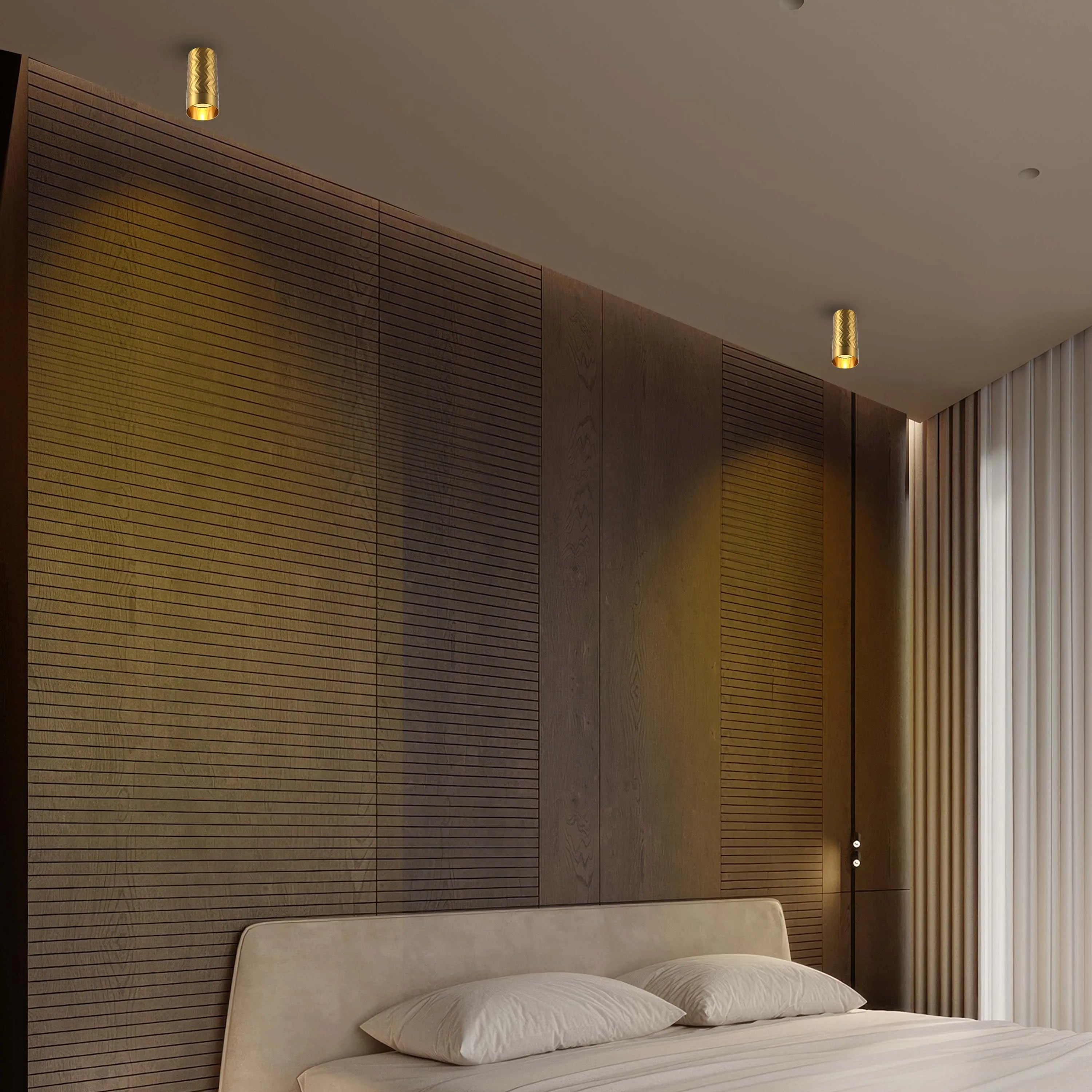 Two modern, brass-coloured, cylinder-shaped lights affixed to the ceiling, illuminating a bedroom with warm light.