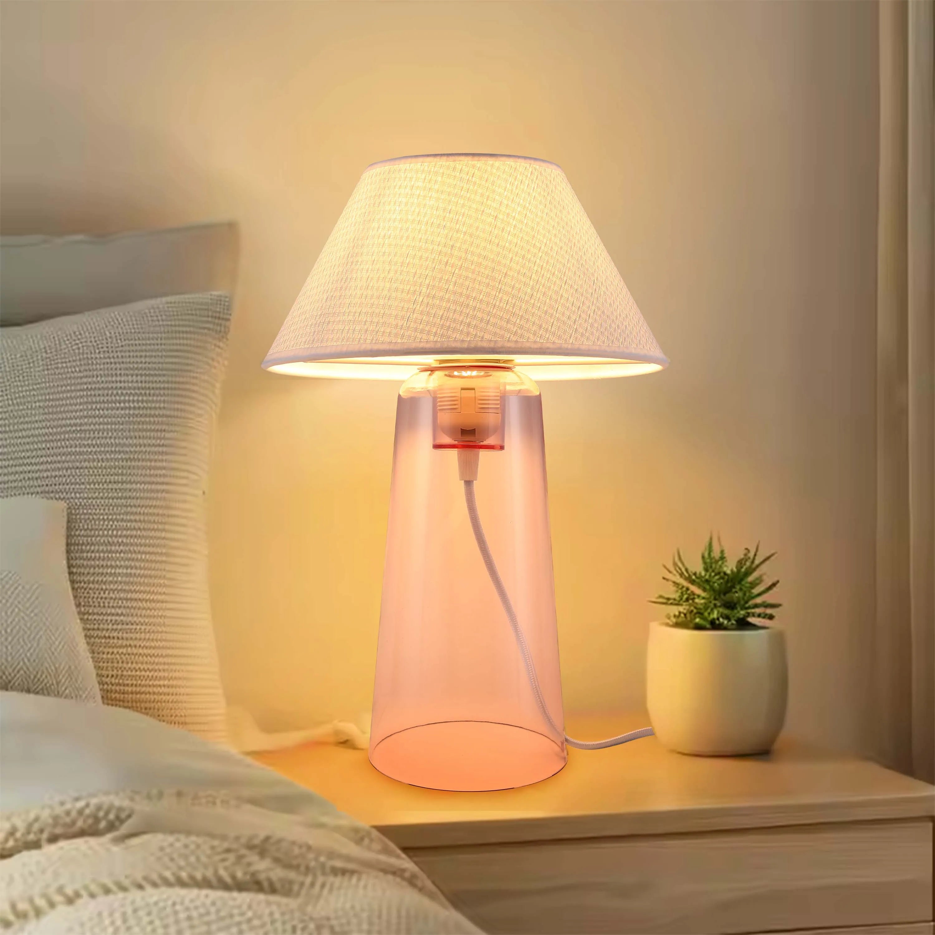 A bedside lamp with a fabric shade and a pink translucent base casts a warm glow onto a wooden bedside table.