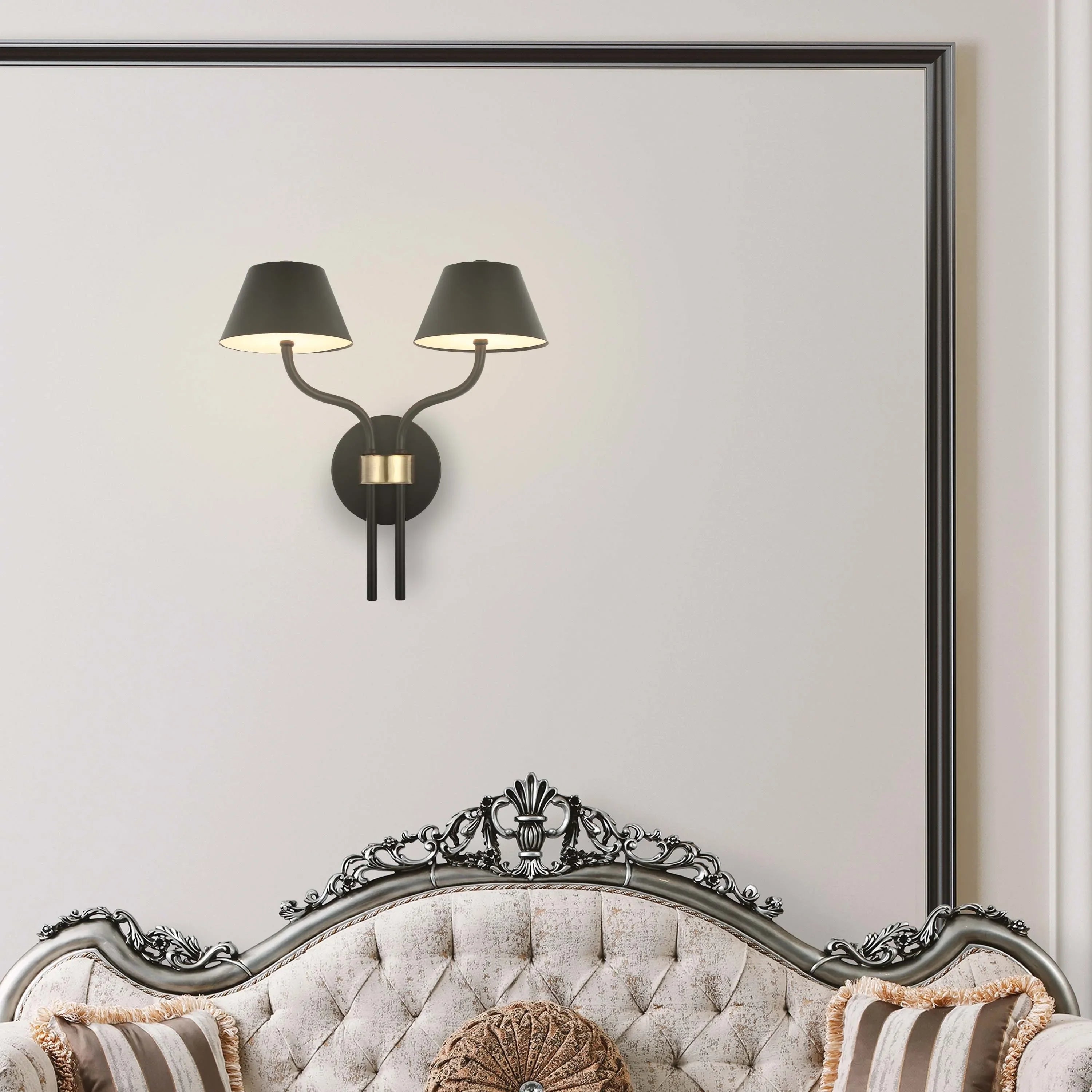 A two-light wall sconce in black and gold, providing a soft, ambient glow in an elegant setting above a chaise lounge.