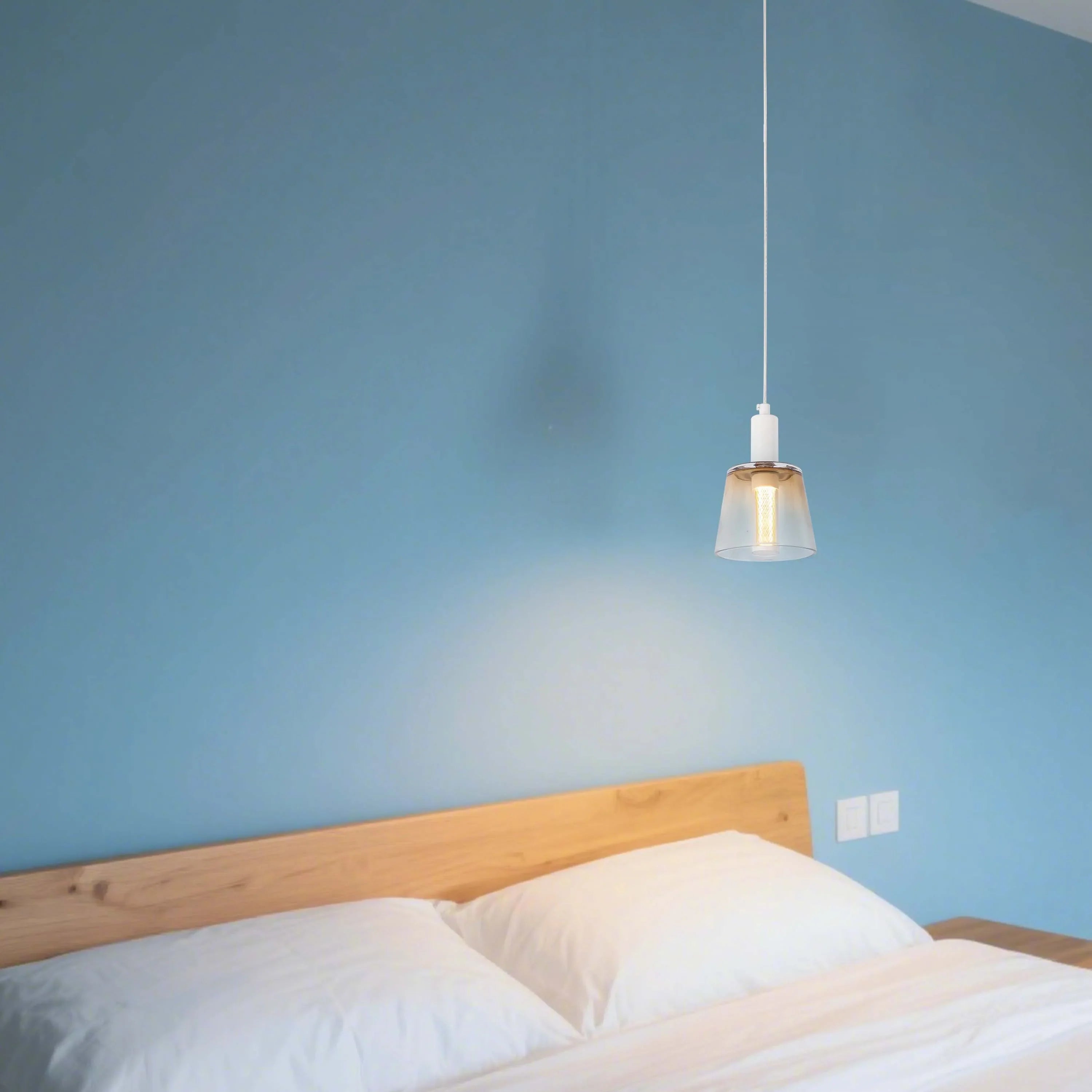 Modern pendant light fixture over a bed, casting a soft, warm glow against a blue wall. Minimalist design for stylish bedrooms.